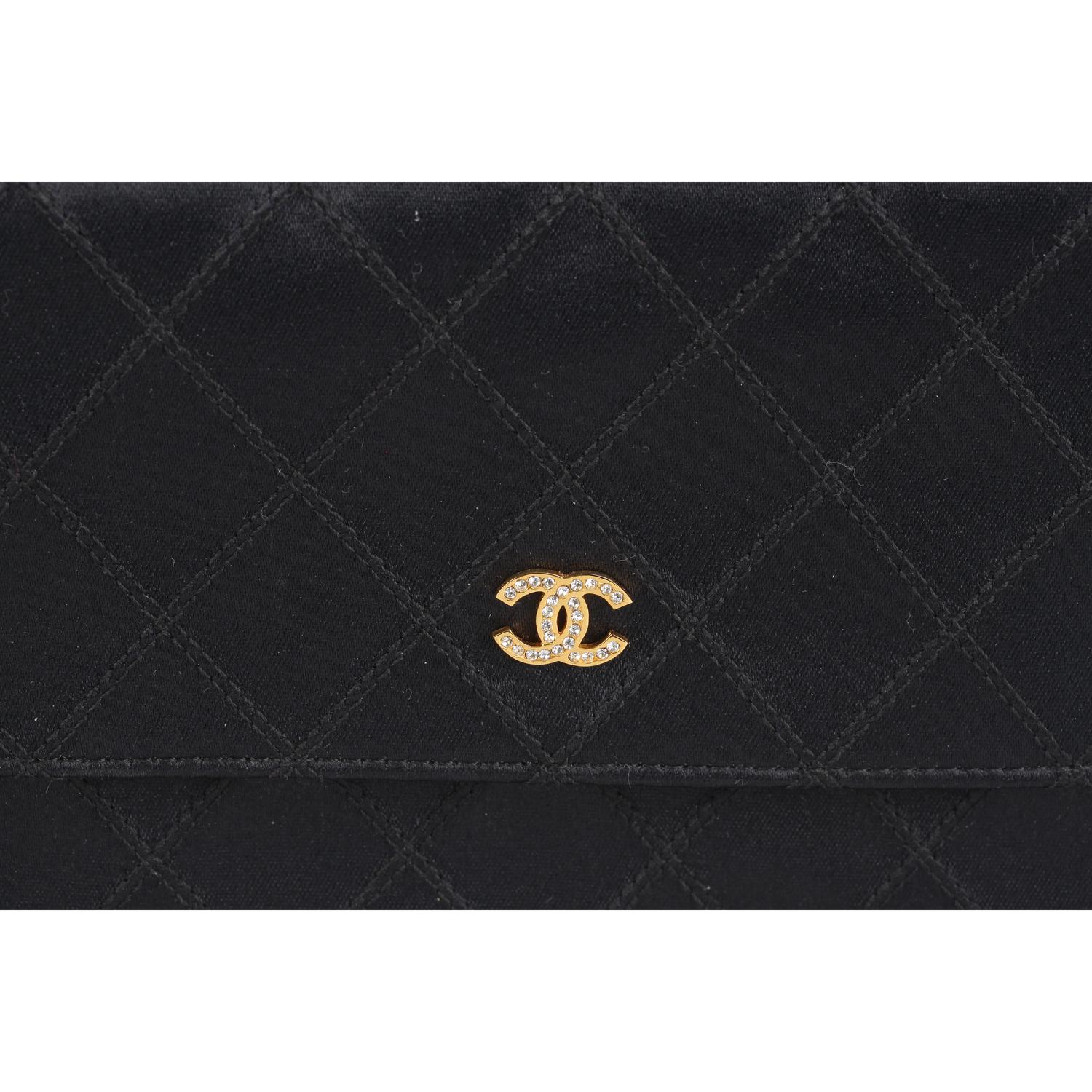 Vintage Chanel black quilted satin small clutch from the late 80s - early 90s. Flap with button closure. Gold metal CC - CHANEL logo on the front embellished with rhinestones. 1 open pocket on the back. Leather and gros-grain lining interior. 1 side