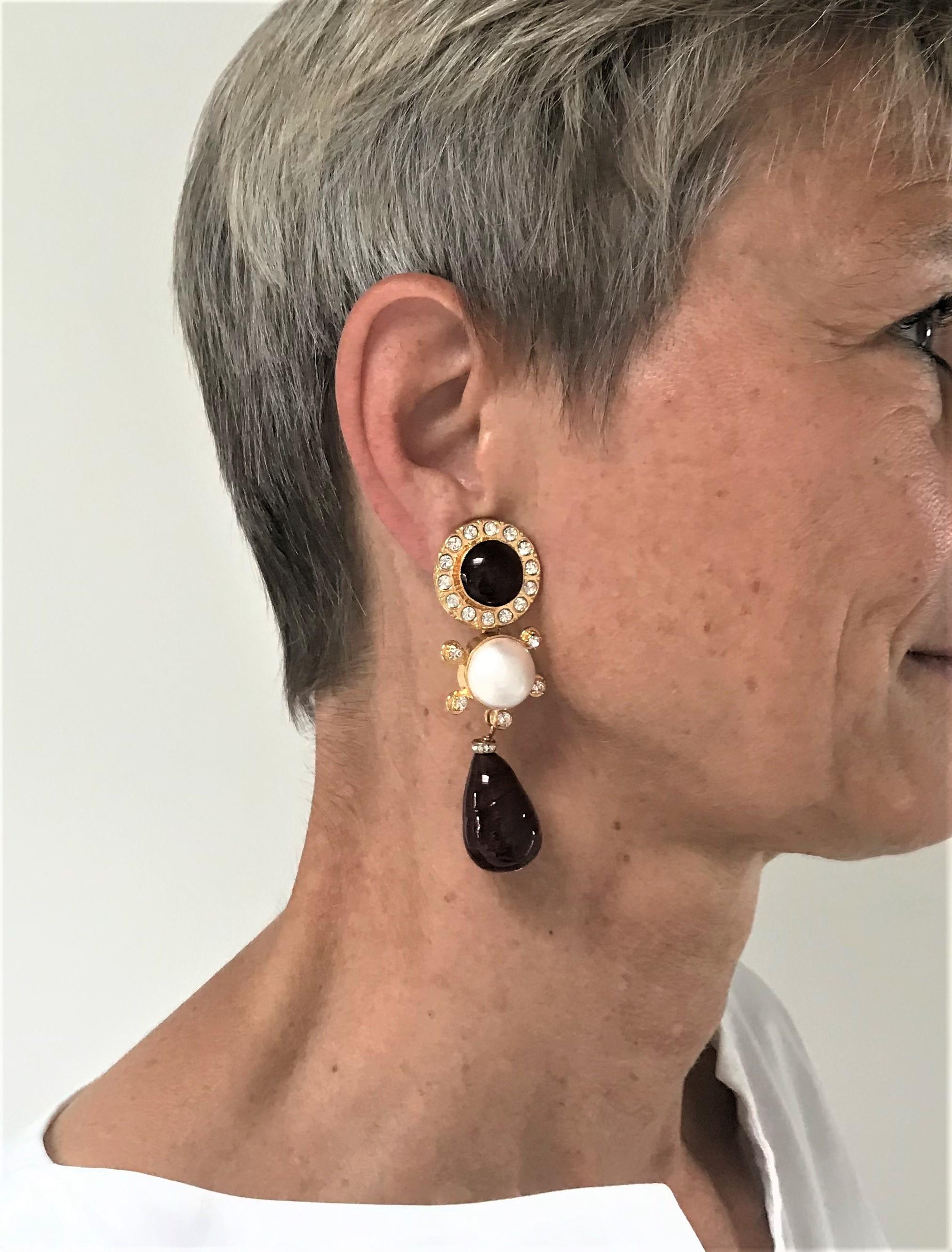 Exceptional Chanel ear clips consisting of 3 parts. Upper part with purple Gripoix glass stone and surrounded by small rhinestones. In the middle, beautiful faux pearl with 5 set rhinestones, hanging from it 2,5 cm red Gripoix drops. Signed from the