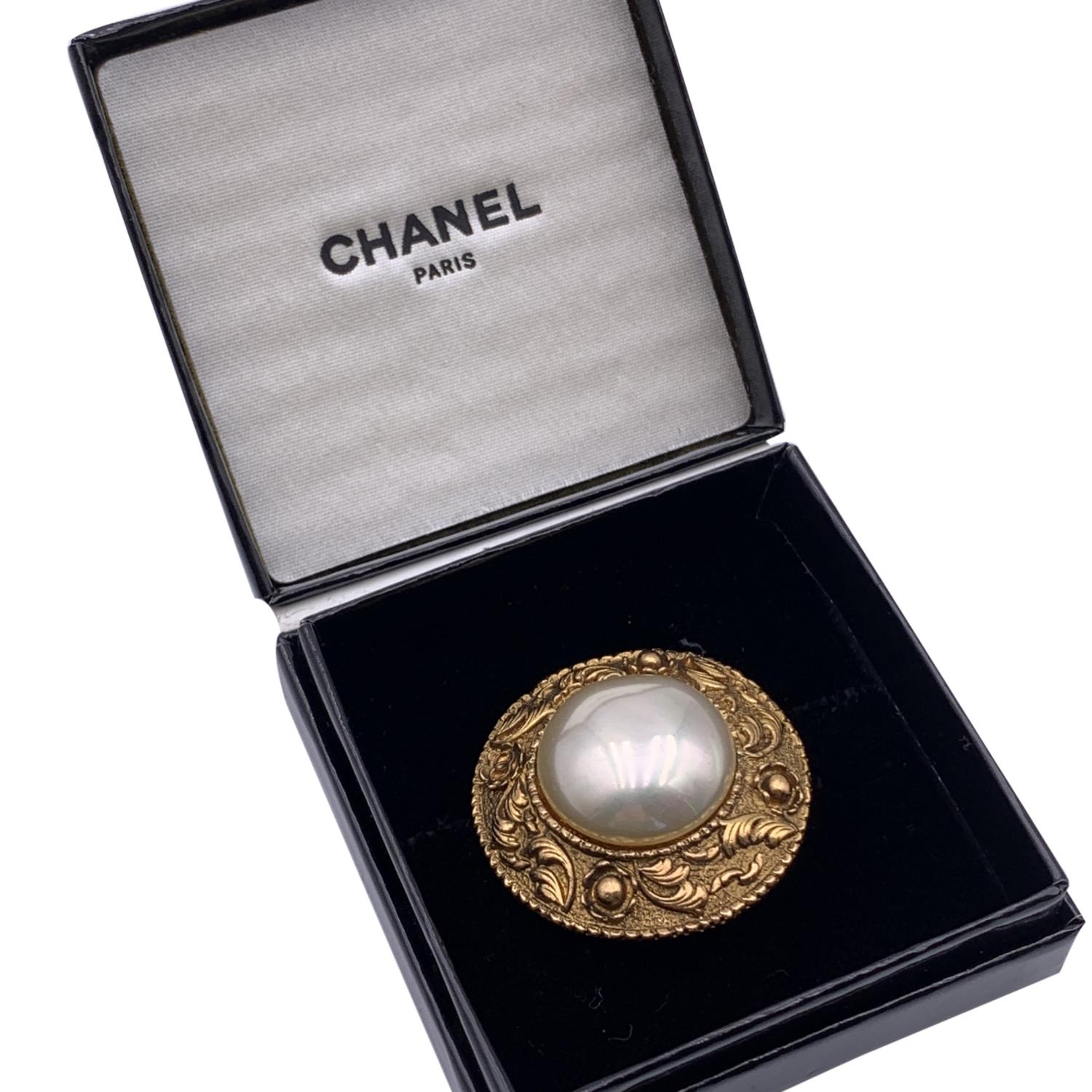 Gold metal Chanel brooch featuring glass pearl cabochon, from the early 90s. CC logo embossed on the metal. Safety pin closure on the back. 'CHANEL 2 CC 6 - Made in France' oval hallmark on the back. Diameter: 1.5 inches - 3.8 cm.

Condition

A -