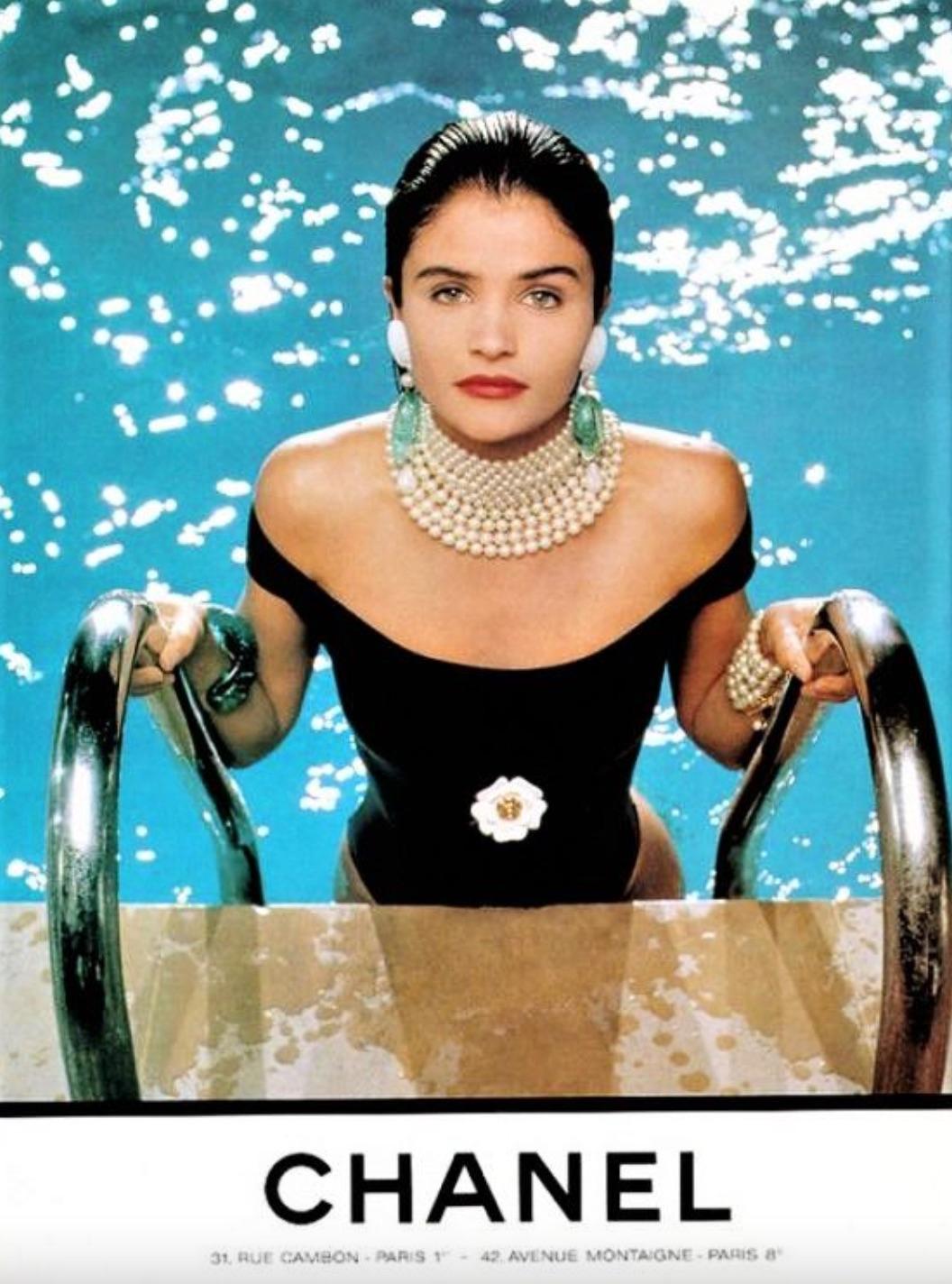 This iconic Chanel swimsuit, as seen on Helena Christensen, is a rare piece from the Spring/Summer 1990 collection. Featuring a scoop neckline, cap sleeves, and a black satin bow, it’s adorned with a sculptural off-white 