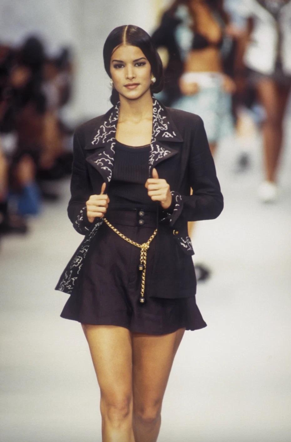 A standout from Chanel’s Spring 1993 runway, this black skirt suit captures the house’s timeless codes with a bold twist. Worn by Patricia Velasquez, the sharply tailored silhouette is crafted from a luxurious blend of linen and silk, punctuated by