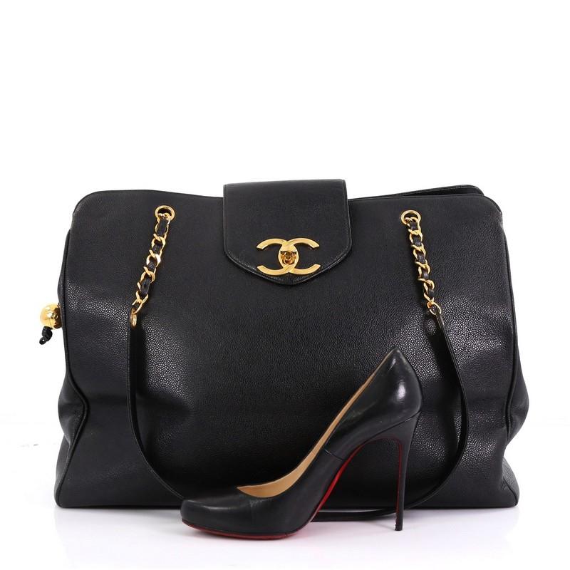 This Chanel Vintage Supermodel Weekender Bag Caviar Large, crafted in black caviar leather, features dual woven-in leather chain straps, protective base studs, and gold-tone hardware. Its CC turn-lock and zip closures open to a black leather