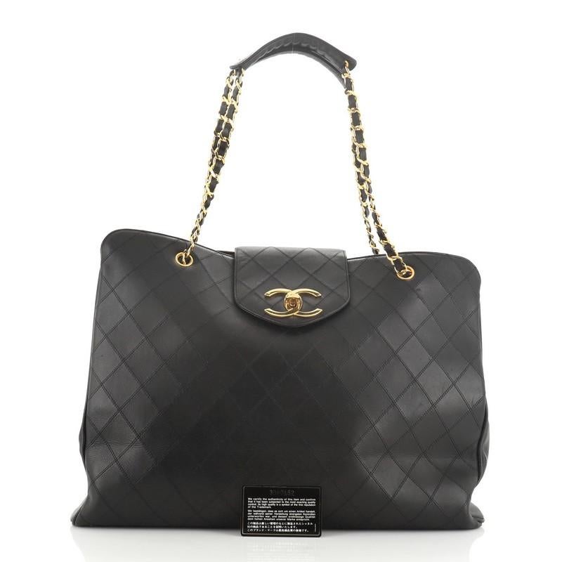 This Chanel Vintage Supermodel Weekender Bag Quilted Leather Large, crafted in black quilted leather, features dual woven-in leather chain straps, flap tab with turn-lock closure, and gold-tone hardware. Its zip closure opens to a black leather and
