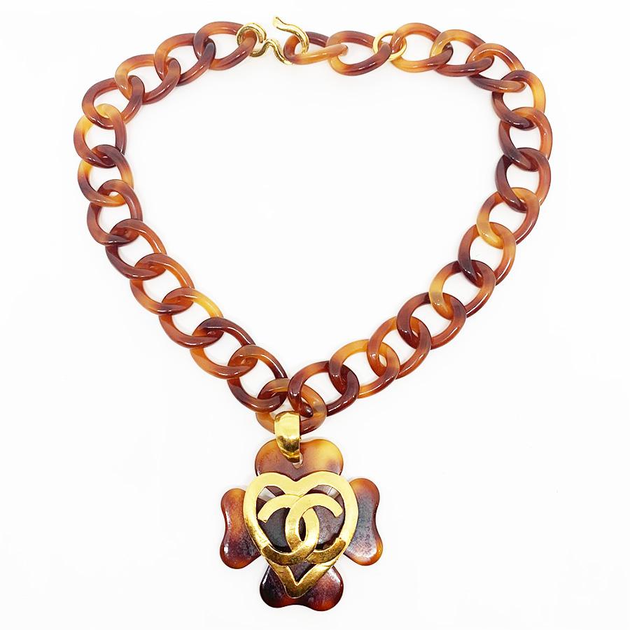 The necklace is signed by Maison CHANEL. It represents a succession of tortoiseshell-style links on which is suspended a four-leaf clover comprising a metal heart gilded with fine gold, which in turn has the initials CC of the brand.
The necklace is