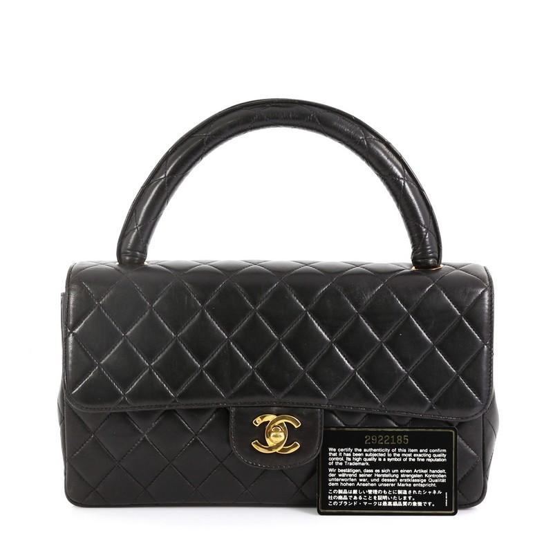 This Chanel Vintage Twin Top Handle Flap Bag Quilted Lambskin Medium, crafted in black quilted lambskin, features a single loop leather handle and gold-tone hardware. Its CC turn-lock closure opens to a red leather interior with zip and slip