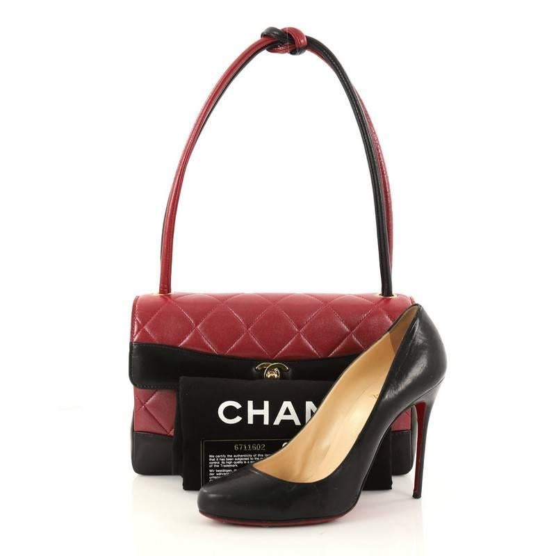 This authentic Chanel Vintage Two Tone Knot Handle Flap Bag Quilted Lambskin Medium exudes a classic yet easy style made for the modern woman. Crafted from red quilted lambskin leather with black leather trims, this elegant flap bag features