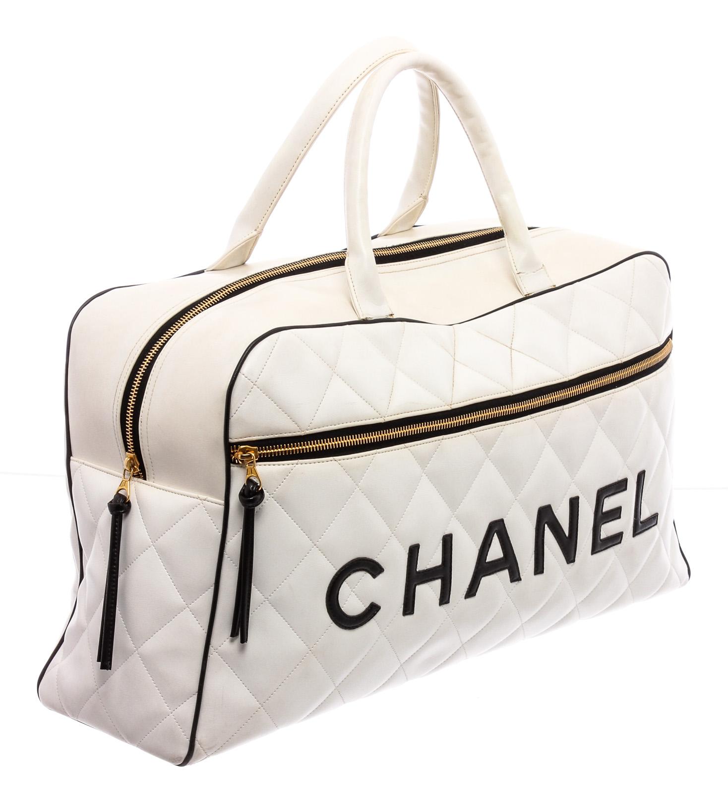 White quilted leather vintage Chanel duffle bag with gold-tone hardware, dual rolled top handles, protective feet at base, black eather trim, single zip pocket and logo at exterior, black leather lining, single interior zip pocket and zip closure at