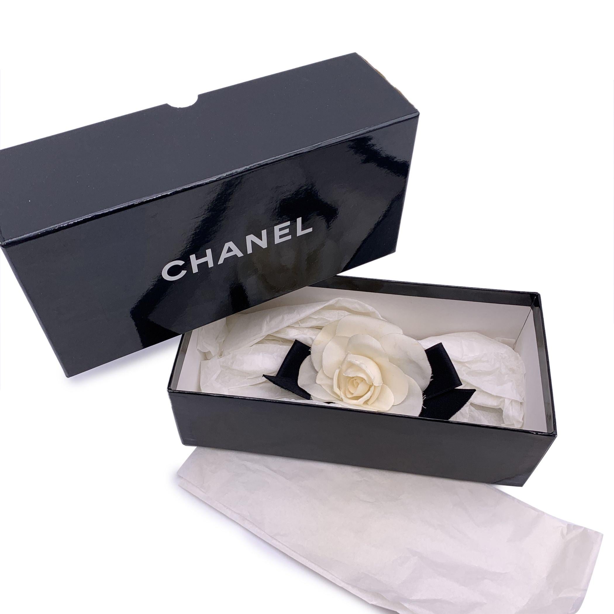 Lovely vintage Chanel brooch. White silk Camellia flower with black satin bow 'Chanel CC Made in France' oval tab on the back. Flower width: 3.5 inches - 8.9 cm. Height: 3.5 inches - 8.9 cm. Condition B - VERY GOOD Gently used. The borders of the