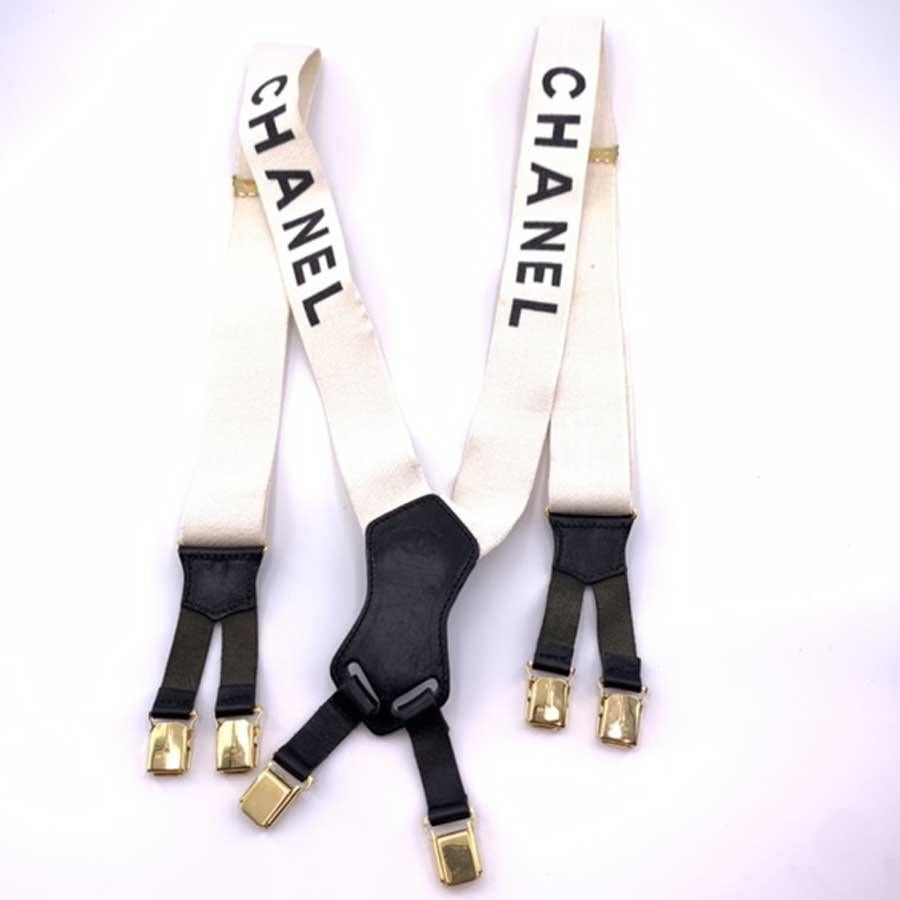 Must-Have very popular with trendy fashion magazines. We present you here beautiful suspenders from Maison CHANEL in white elastic fabric on which is inscribed, the brand CHANEL in black letters. We have black leather and gold metal on the