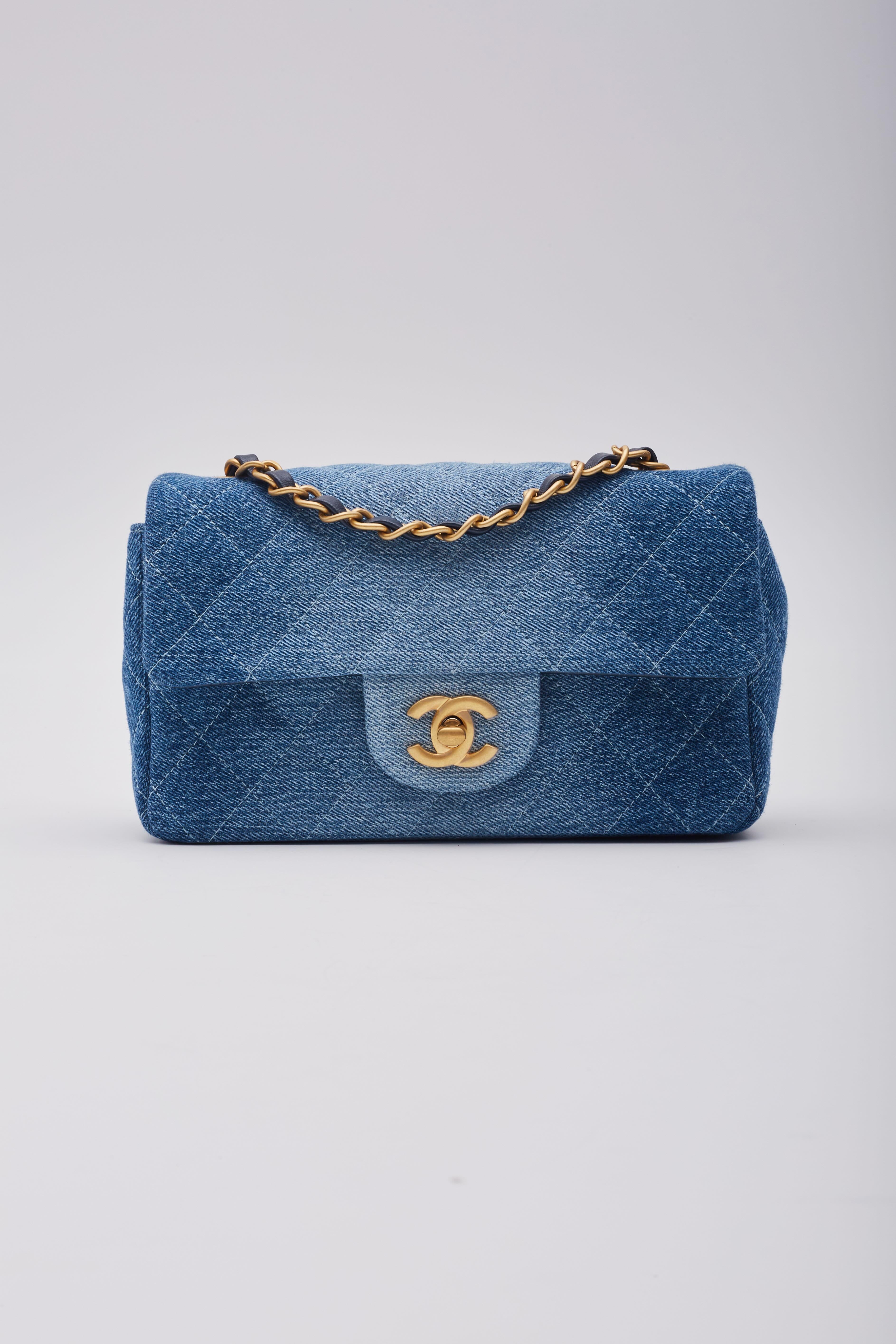 This Chanel mini rectangular flap bag is constructed of soft quilted blue washed denim. It features a gold chain-link shoulder strap threaded with denim, a rear patch pocket, and a gold classic CC turn-lock closure. The flap opens to a blue leather