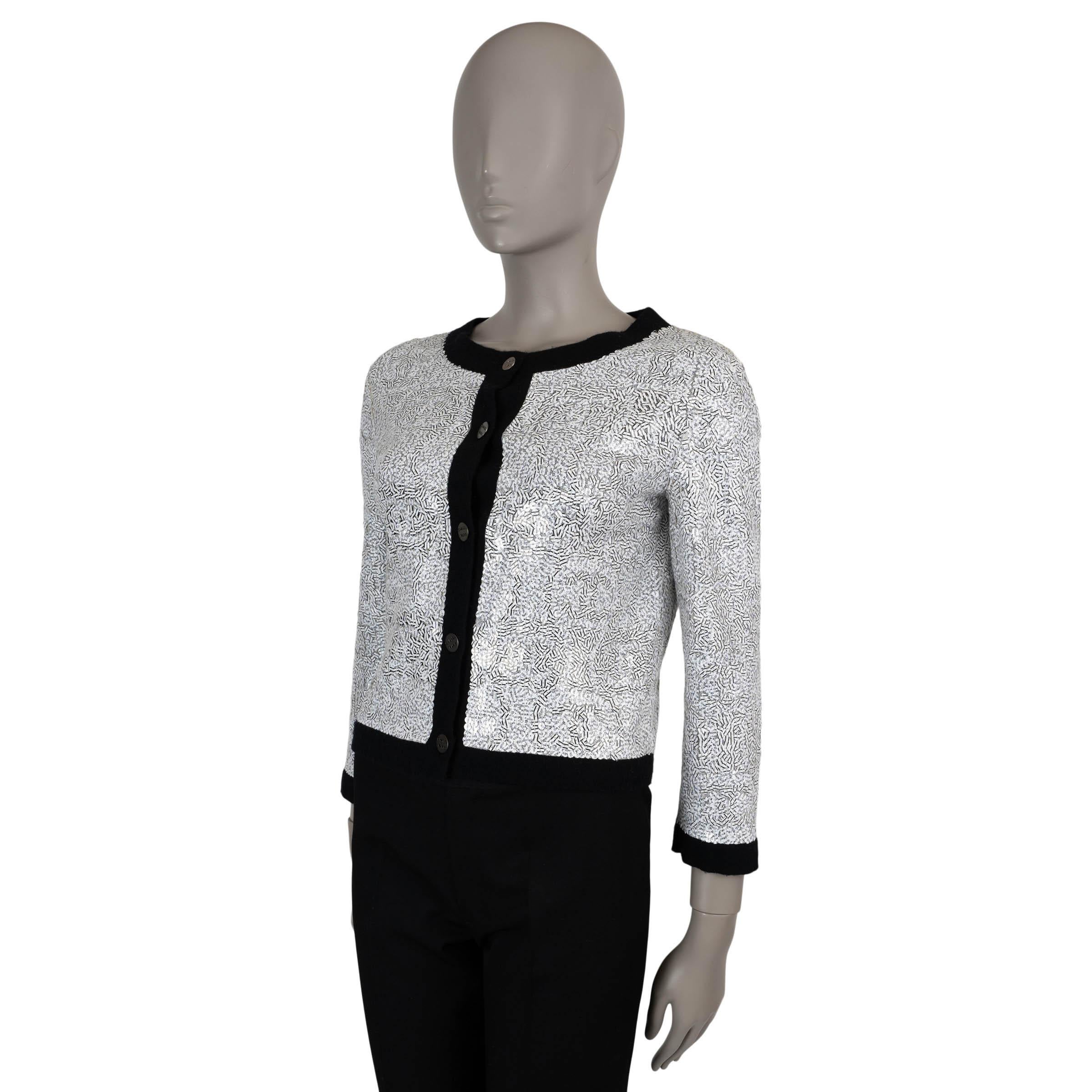 This 100% authentic Chanel cardigan in white cashmere (please note the content and size tag are missing) is fully adorned with white sequins, creating a striking contrast with black stripes and typefont writing. Designed with a cropped silhouette,