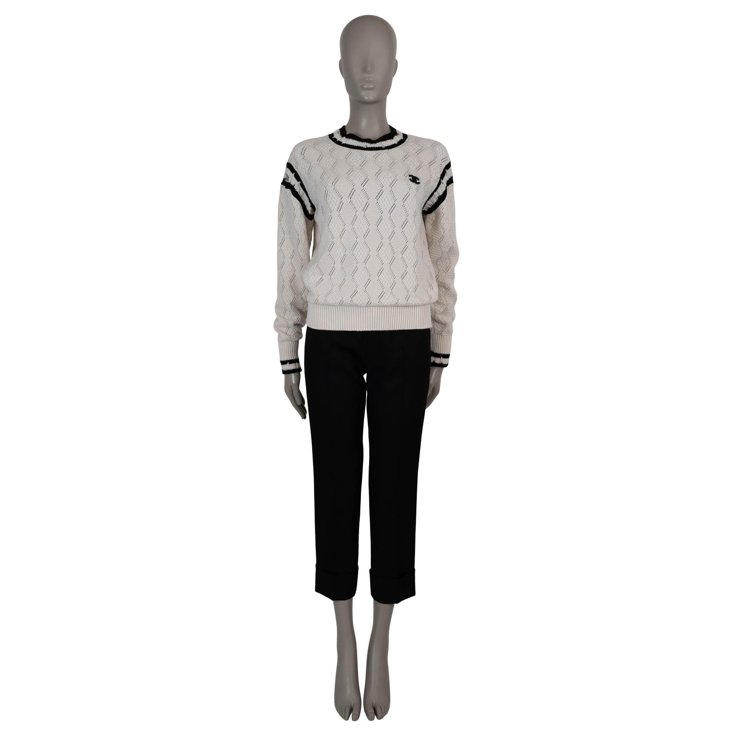Este jersey 100% auténtico de Chanel en punto jacquard blanco y negro de cachemira (99%) y elastano (1%) combina una textura intrincada con toques deportivos. Con un corte ligeramente extragrande, tiene detalles de punto calado, rayas negras,