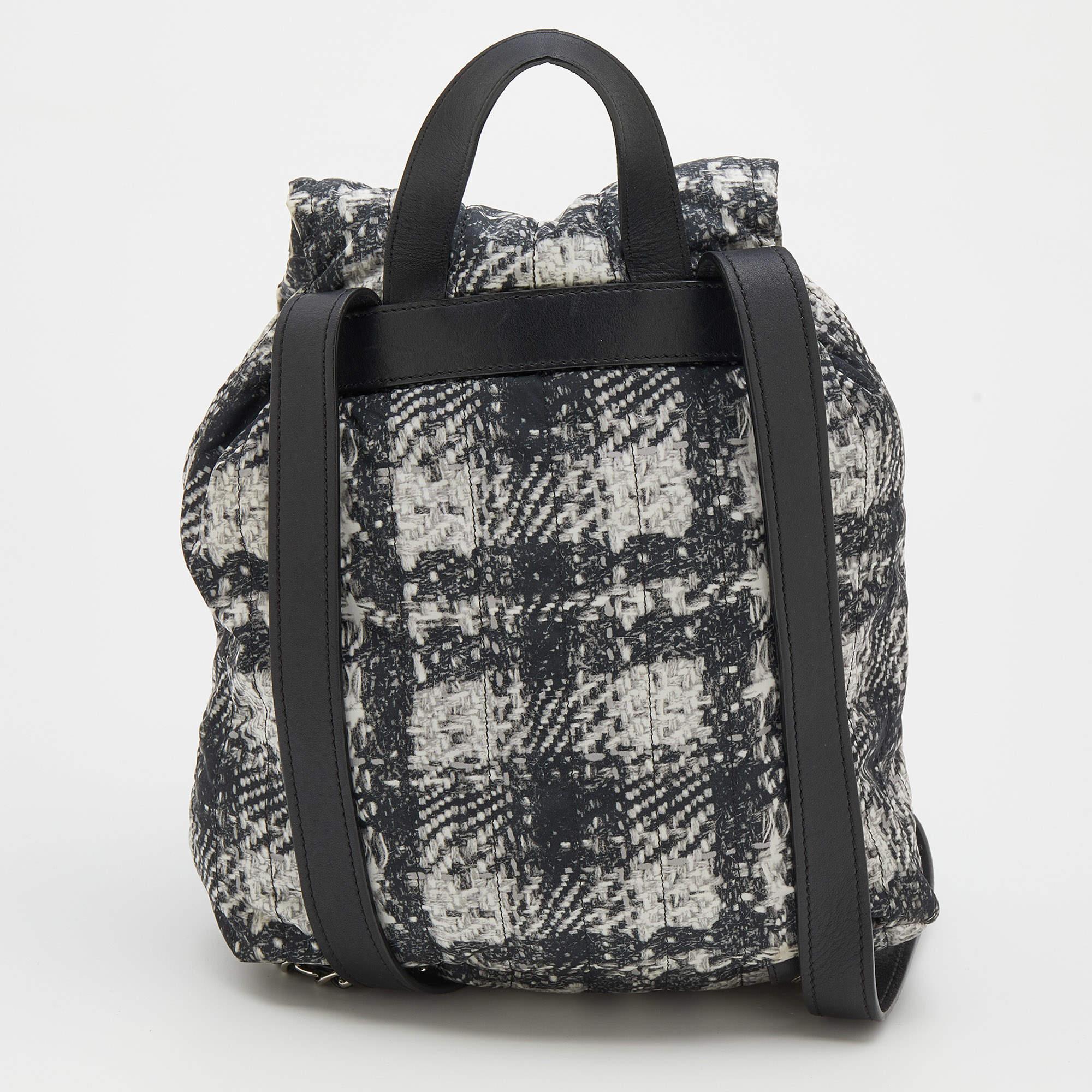 The drawstring enhances the silhouette of this Chanel backpack. Crafted from tweed-printed nylon, it signifies luxury and fashion. The 'CC' motif on the front adds a signature accent to it, and its exterior is equipped with a front zipper pocket. To