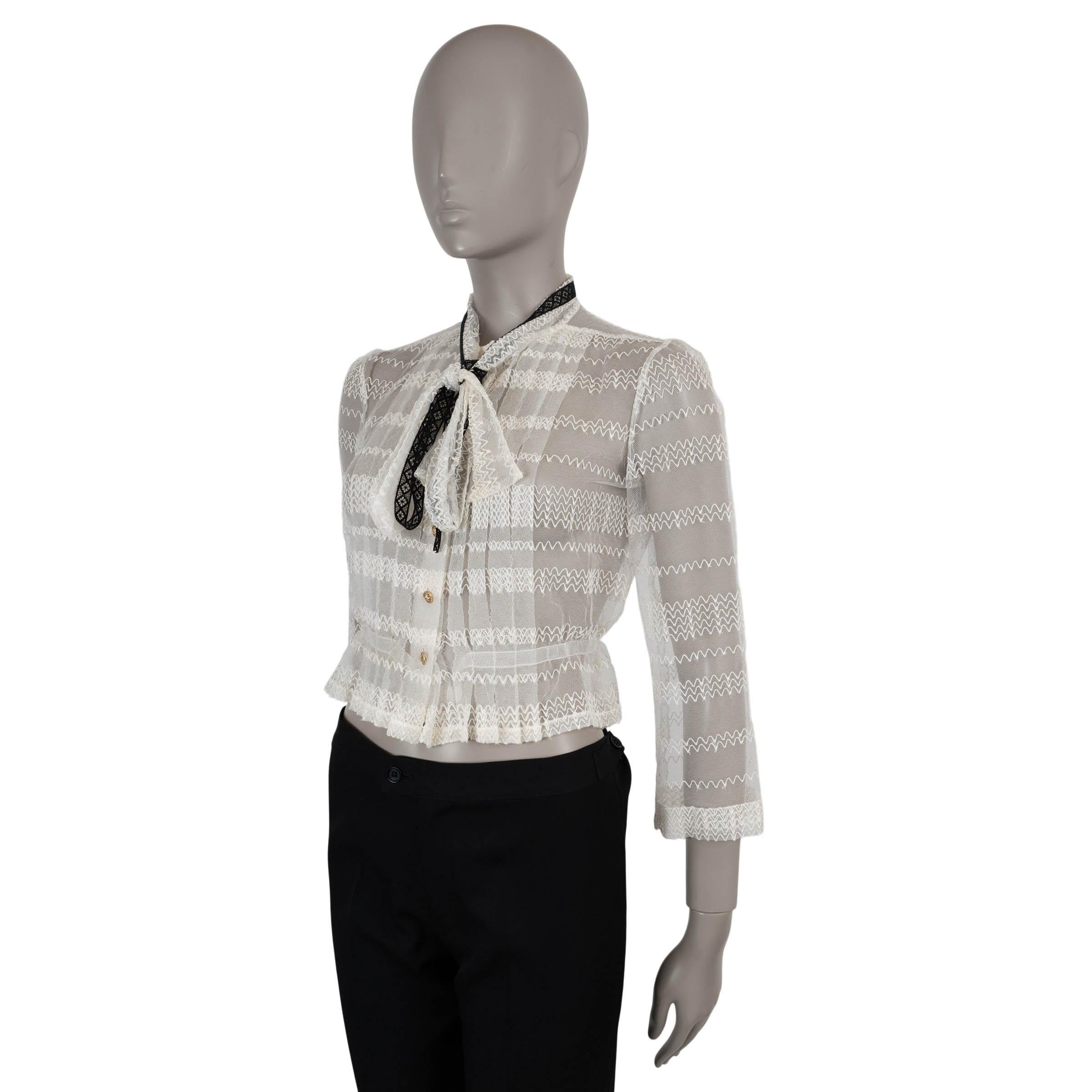 Cette blouse 100% authentique de Chanel est confectionnée dans une délicate maille blanc cassé à partir d'un mélange raffiné de coton (58%), de soie (23%) et de nylon (19%), brodée de rayures ondulées en zigzag. La silhouette courte est rehaussée