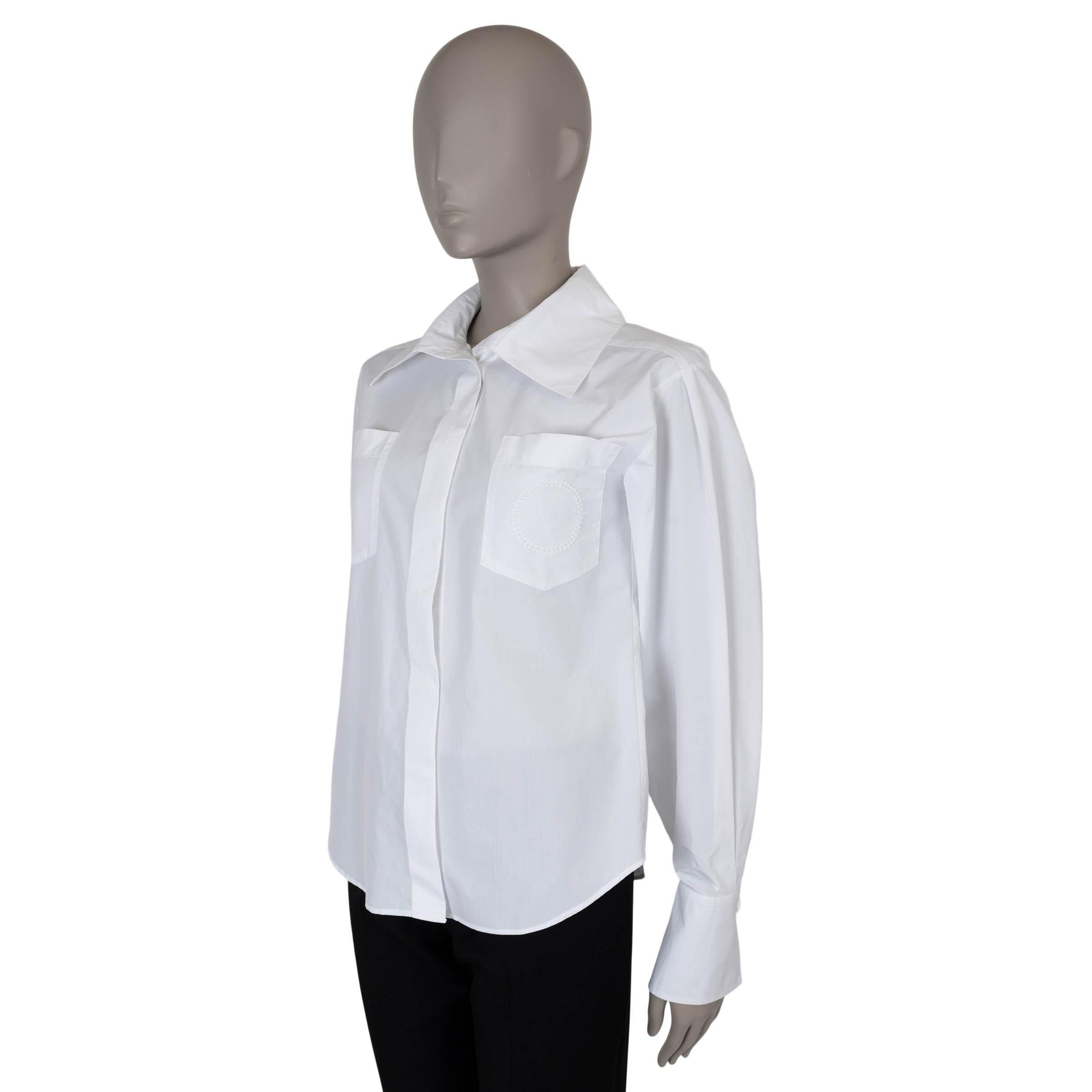 This 100% authentic Chanel button-up shirt is crafted from crisp white poplin cotton and features a wide collar, buttoned cuffs, and two chest pockets adorned with subtle logo embroidery. The shirt closes with concealed buttons on the front for a