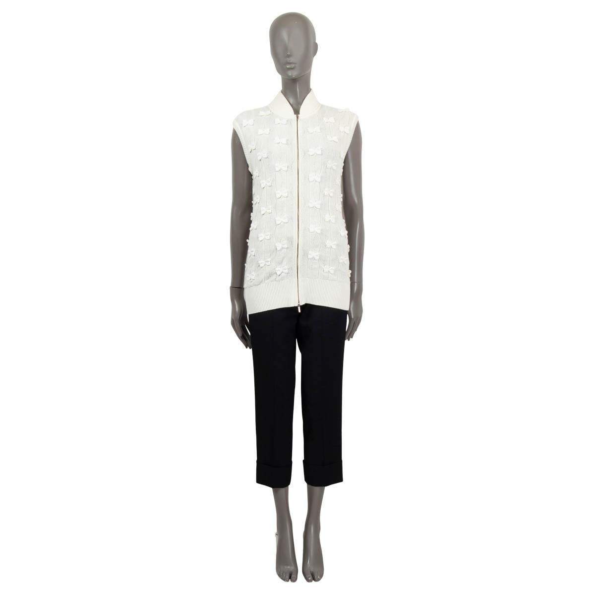100% authentic Chanel knit vest in ivory colored cotton (63%), polyamide (36%) and elasthanne (1%). Features little embellished bows in ivory, a ripped stand-up collar and opens with a silver zipper in the front. Has been worn and is in excellent