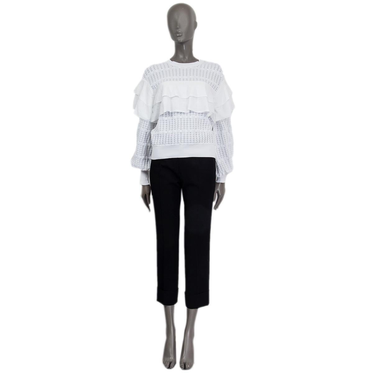 100% authentic Chanel tiered knit sweater in off white cotton (100%) embellished with ruffels on the front, the back and on the shoulders. The sweater is slightly transparent and opens with a creme/white CC button on the back. Has been worn and is