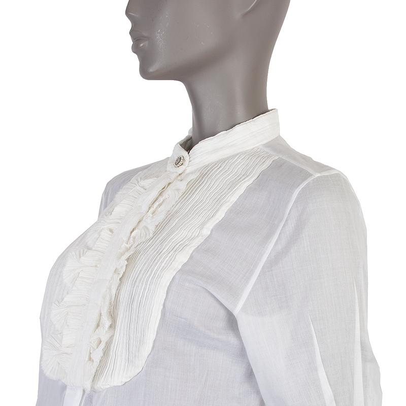 Chanel 3/4-sleeves shirt in white light cotton (assumed as tag is missing). With pleated band collar, pleated bib, fan ruffles on the front. one-button square cuffs, and side slits. Closes with one rhinestones and pearls button and concealed buttons