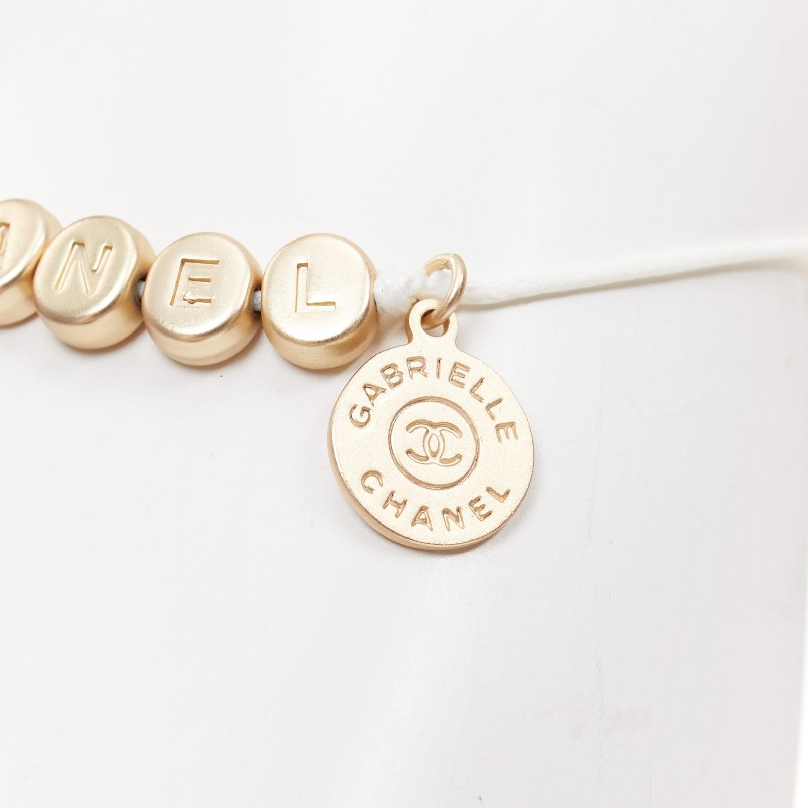 CHANEL brazalete de la suerte con logotipo en tono dorado blanco abalorio de letra de hilo blanco en Excelente estado para la venta en Hong Kong, NT