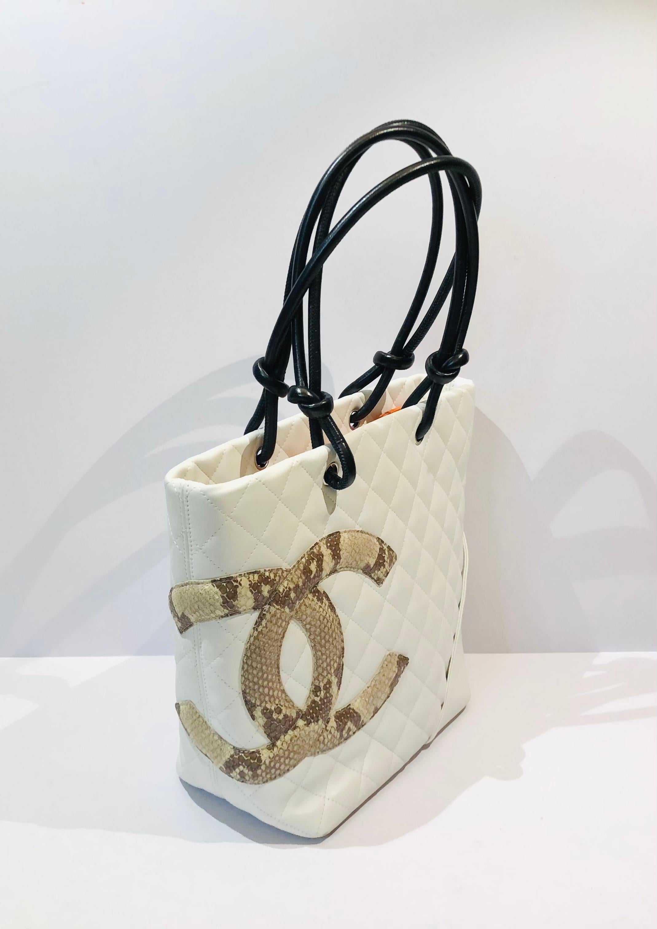 
- Chanel white lambskin quilted tote bag with embossed snakeskin “CC” logo.

- Orange “CC” satin lining with zip closure. 

- Exterior slip pocket. 

- Two interior zip pockets 

- Length: 20cm.
- Height: 24cm.
- Width: 11cm. 
- Handle Drop: 21cm. 