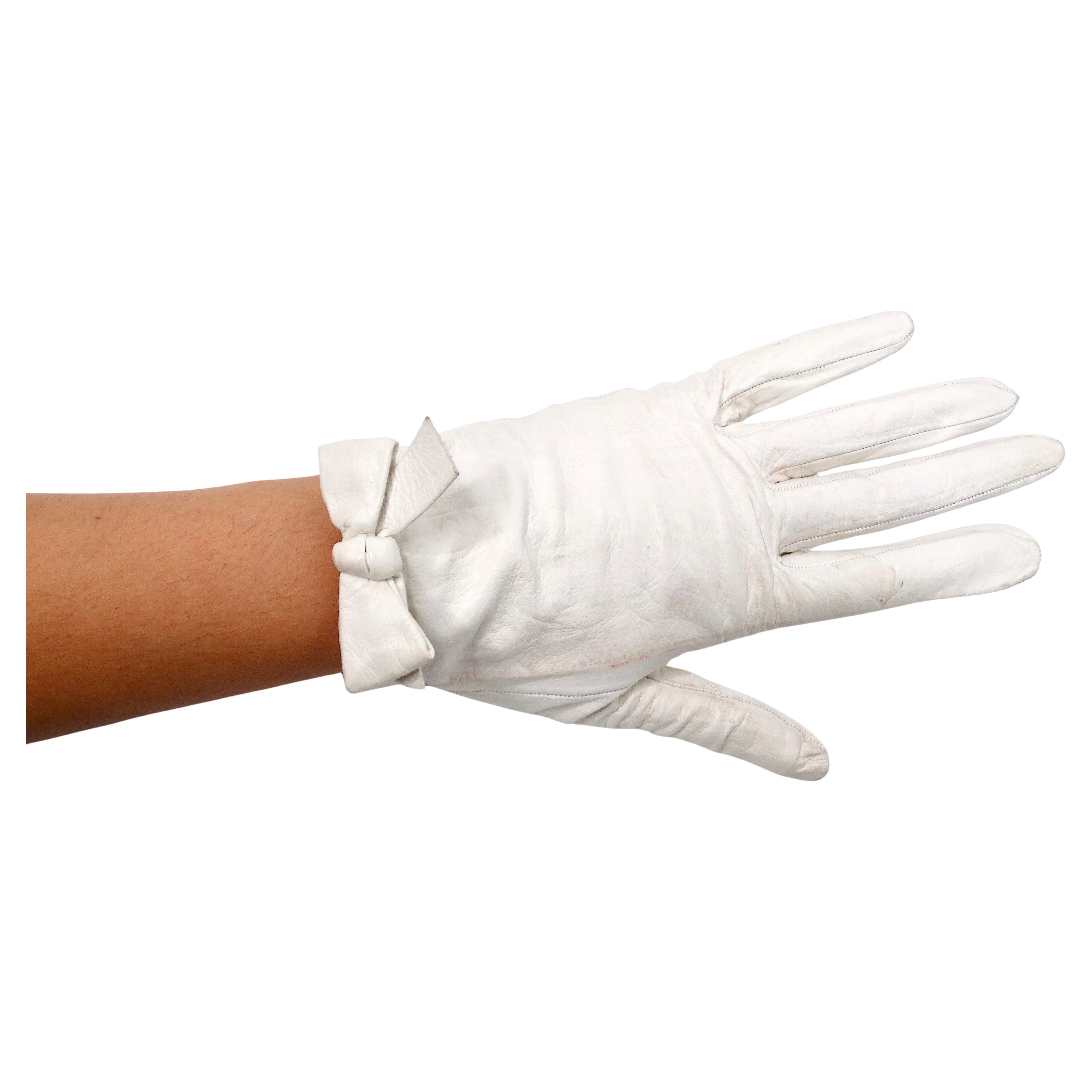The Chanel White Leather Bow Detailed Gloves from the circa 1990s epitomize timeless elegance and luxurious craftsmanship. Crafted from white leather, these gloves exude sophistication, while the delicate bows positioned near each wrist add a