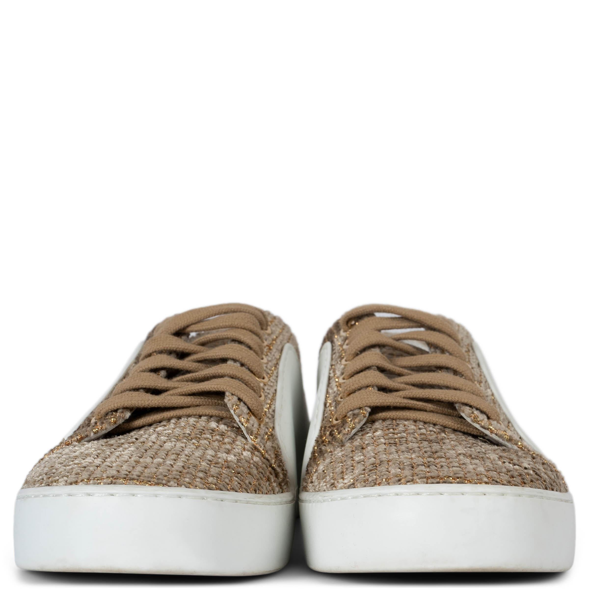 These 100% authentic Chanel low-top sneakers feature a beige and gold lurex tweed upper, complemented by sleek white leather sides and soles. The design is finished with CC embossing on the side, offering a touch of iconic Chanel elegance to these