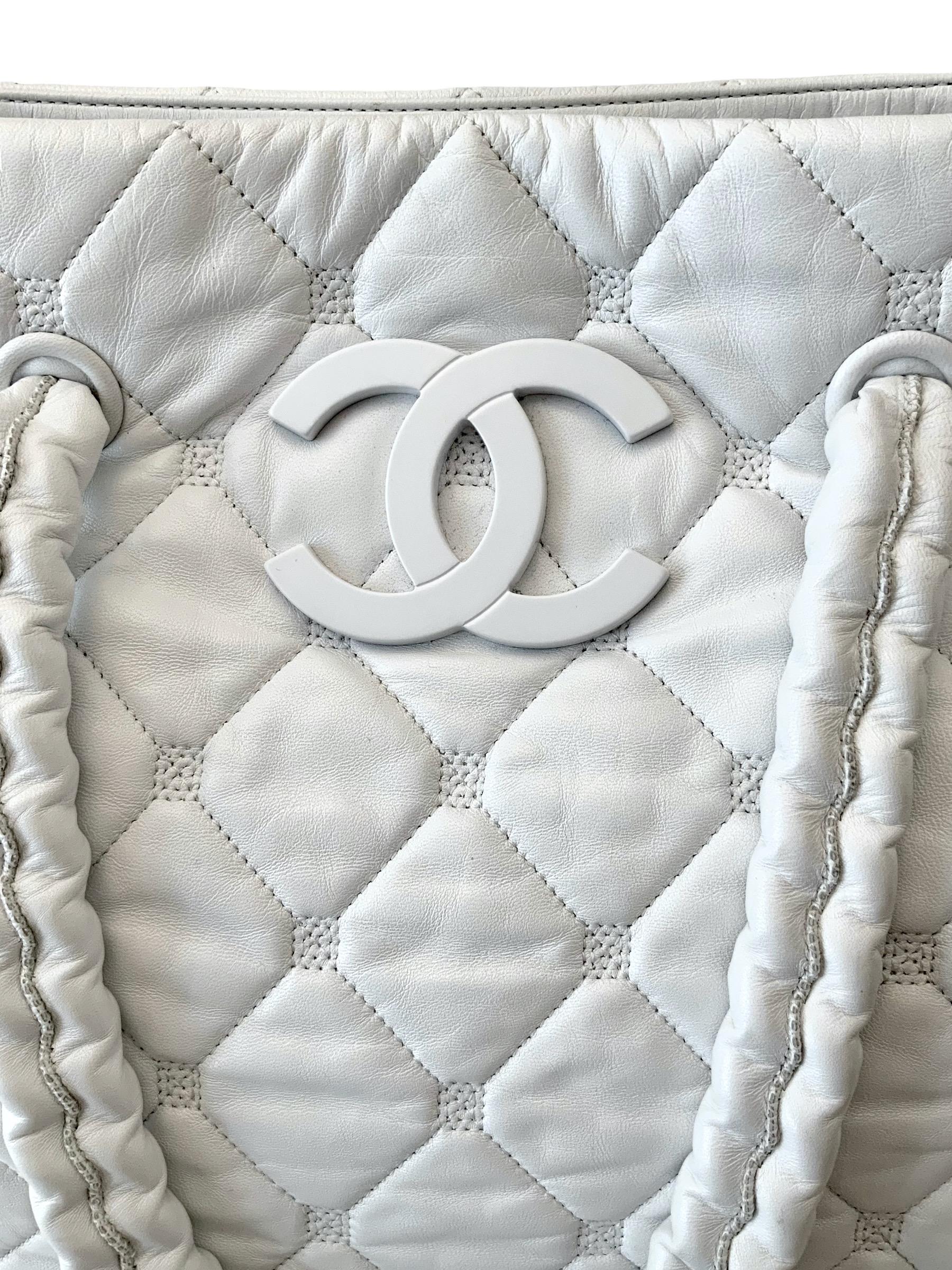 This pre-owned white lambskin leather tote bag from the Chanel 2008 Collection is a hard piece to find especially in such good condition. 
It features a diamond quilted lambskin leather with leather covered 