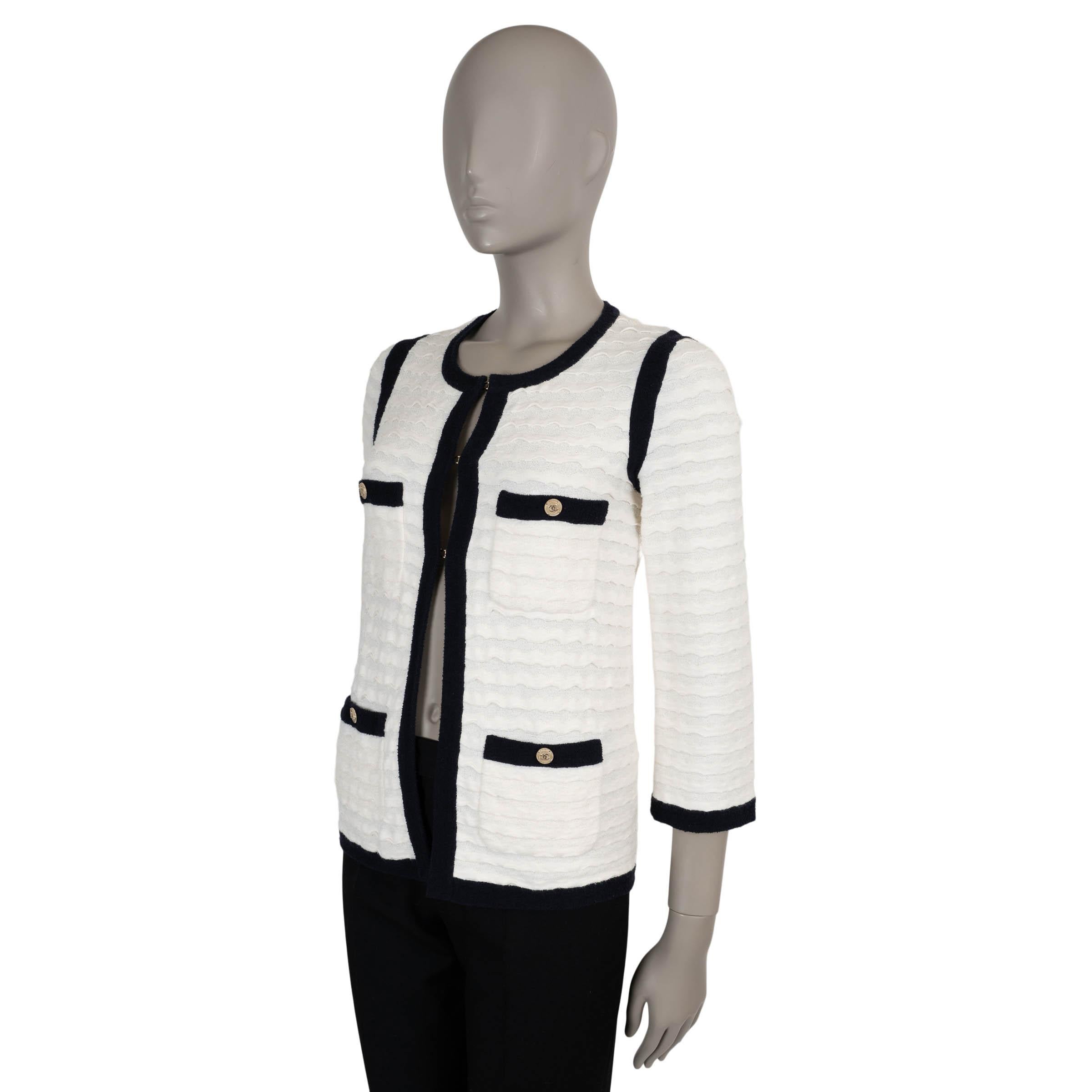 Esta chaqueta de punto 100% auténtica de Chanel reinterpreta los códigos clásicos de la casa con un toque juguetón y texturizado. Confeccionado en punto jacquard de rayas onduladas color crema en una lujosa mezcla de algodón (74%), nailon (16%) y