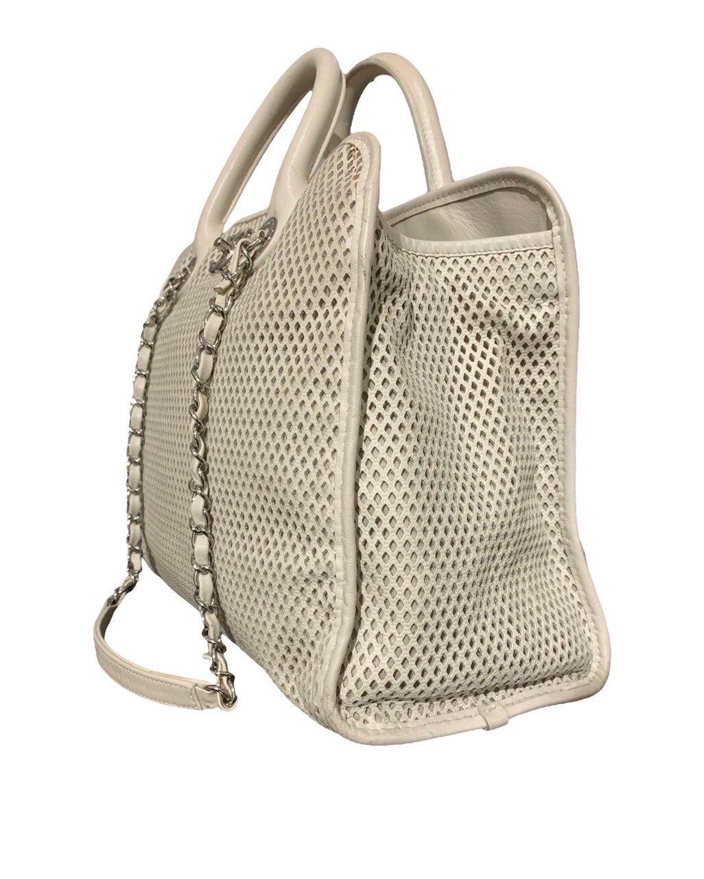 

Chanel signed bag, made of white perforated leather with silver hardware. Equipped with a double rigid leather handle and two braided leather and chain handles to wear the bag on the shoulder. Internally lined in beige canvas, it has various