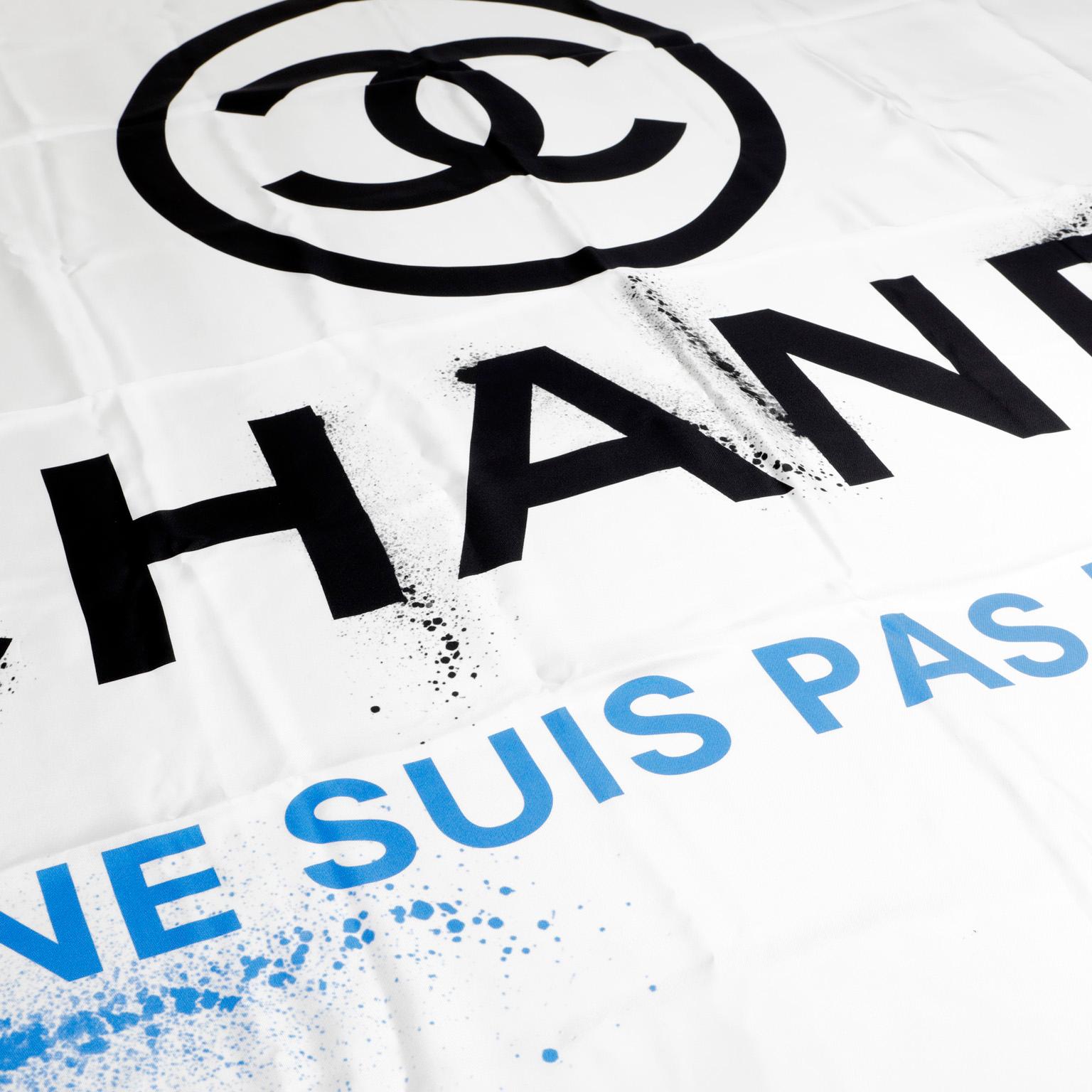 This authentic Chanel White Silk Je Ne Suis Pas En Solde Scarf is in pristine condition.  White silk blend scarf with black Chanel lettering and logo with spraypainted effect.  Je Ne Suis Pas En Solde (“I am not on sale”) in blue. 100% silk. Made in
