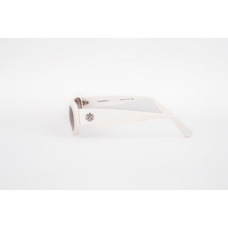 Chanel  - (Made in Italy) White sunglasses with tinted glasses and ornamented with a silvery metal cc logo and camellia on the arm.

Additional information:
Condition: Good condition
Dimensions: Length: 14 cm

Seller Reference: ACC149
