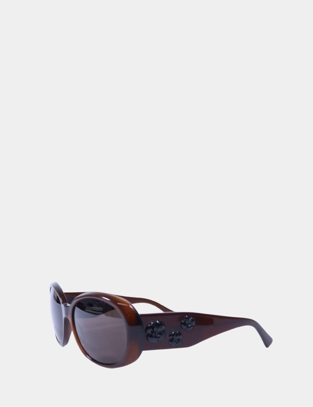 La elegancia atemporal se une a la feminidad juguetona en estas gafas de sol ovaladas marrones de Chanel. Confeccionada en acetato brillante, esta silueta oversize se acentúa con los característicos apliques de flores de camelia negras en las