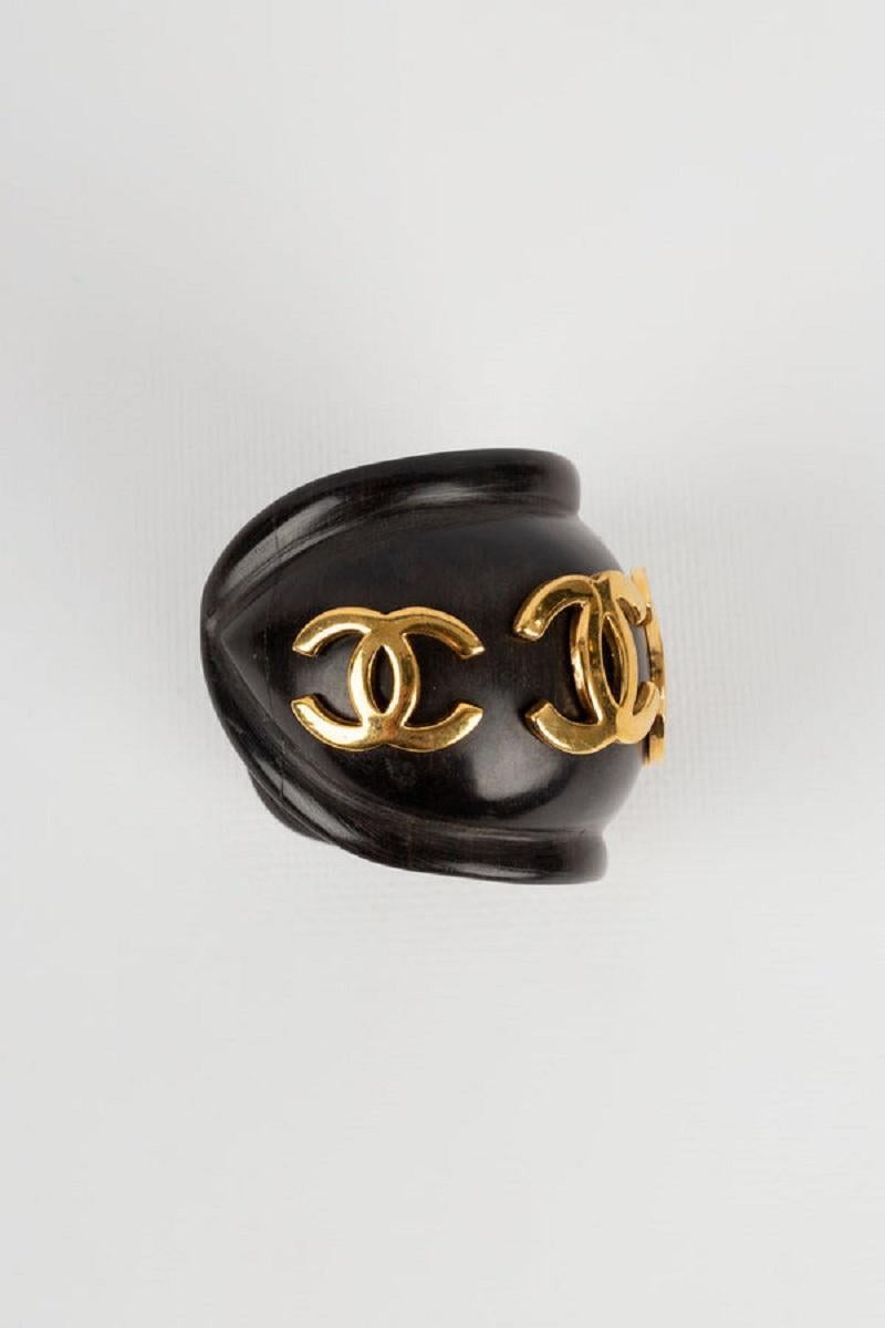 Chanel -(Made in France) Bracelet en bois décoré du logo cc en métal doré. Collection 2cc8 du début des années 1990.

Informations complémentaires :

Dimensions : 
Circonférence : 12 cm 
Ouverture : 3 cm 
Largeur : 5 cm

Condit : Très bon