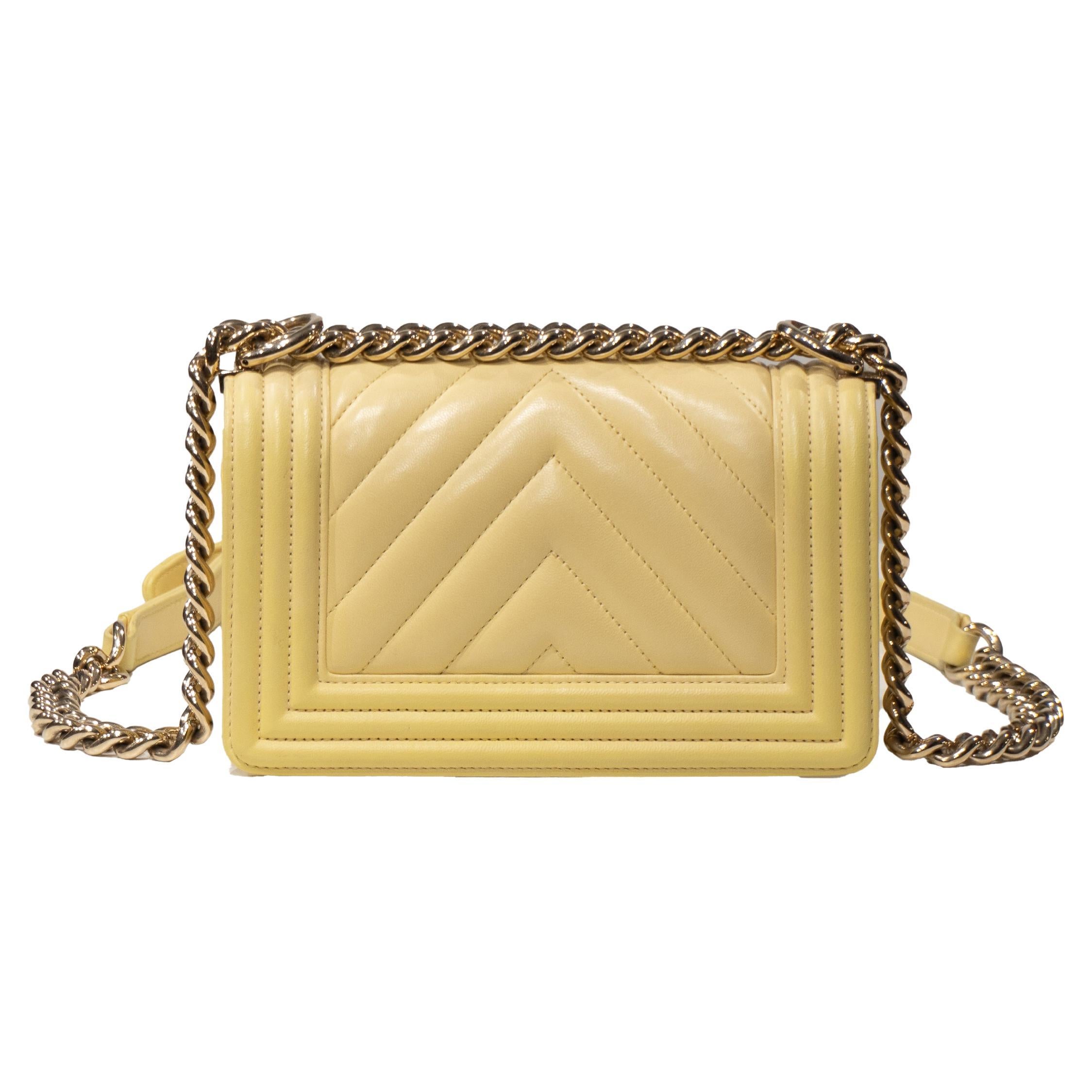 
This small Boy bag is made of yellow herringbone lamb leather with light gold hardware and features a front flap complete with the Le Boy CC push button closure and a light gold tone-on-tone chain link and shoulder strap upholstered in yellow