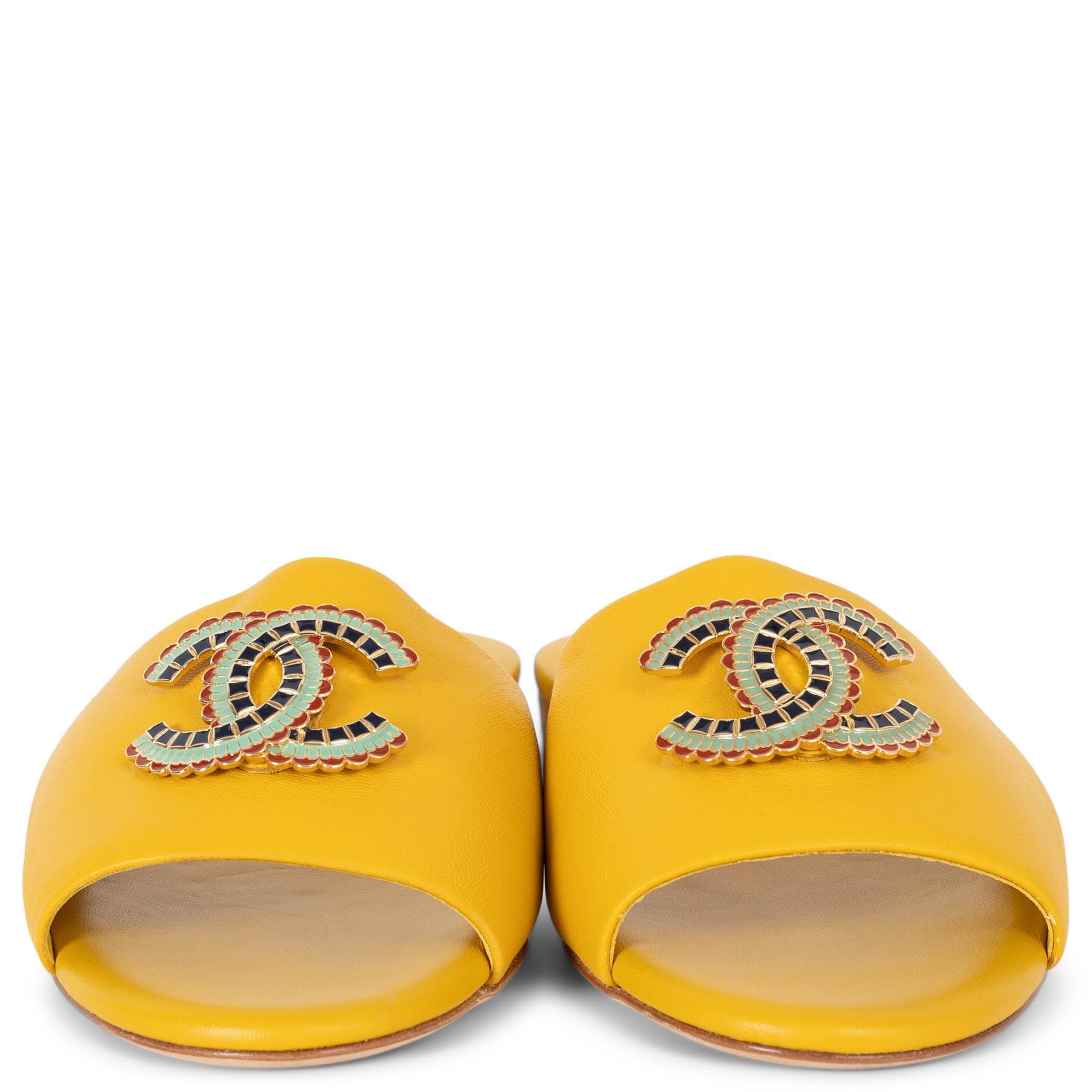 These 100% authentic Chanel slide sandals in yellow lambskin exude effortless elegance with a nod to ancient Egypt. They feature a wide band adorned with an enamelled CC emblem in vibrant shades of red, aqua, and navy blue. Designed with rounded