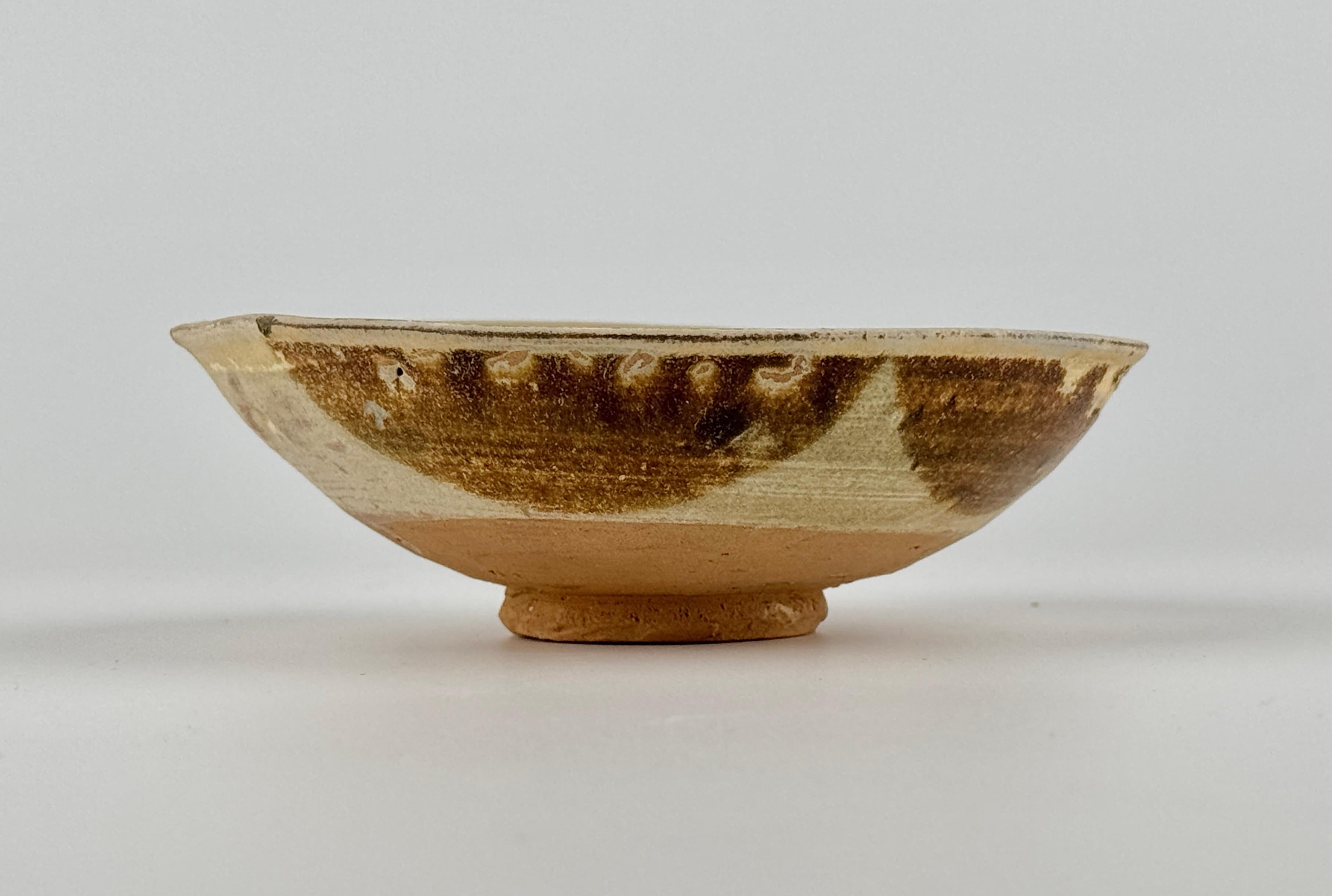 The back side edges have been dipped in four places with brown, probably iron-oxide. The well of the bowl is freely painted in deep green and coffee coloured brown. These are characteristic features of Changsha ware. The Asian Civilisations Museum