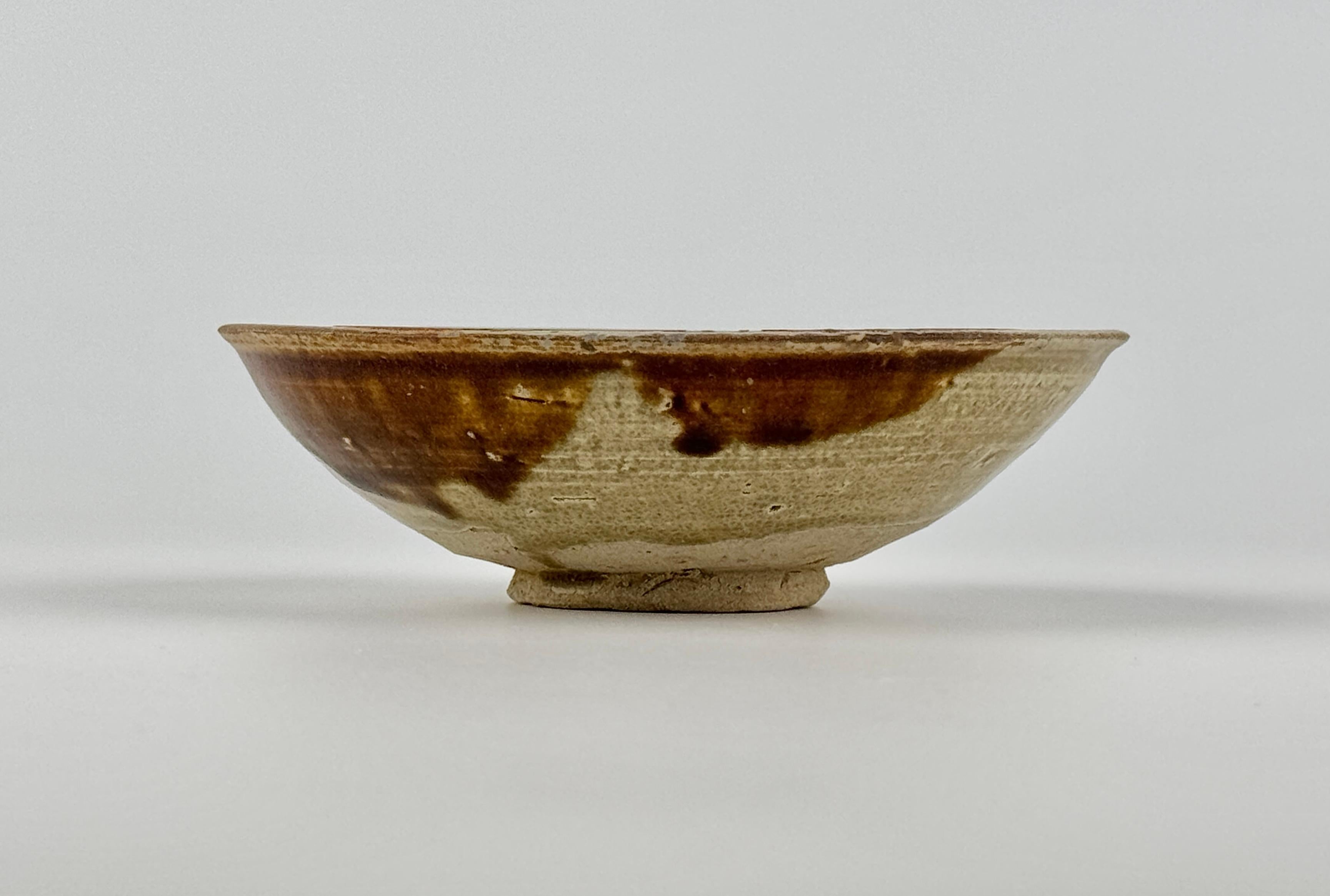 The edges have been dipped in four places with brown, probably iron-oxide. The well of the bowl is freely painted in deep green and coffee coloured brown. These are characteristic features of Changsha ware. The Asian Civilisations Museum in