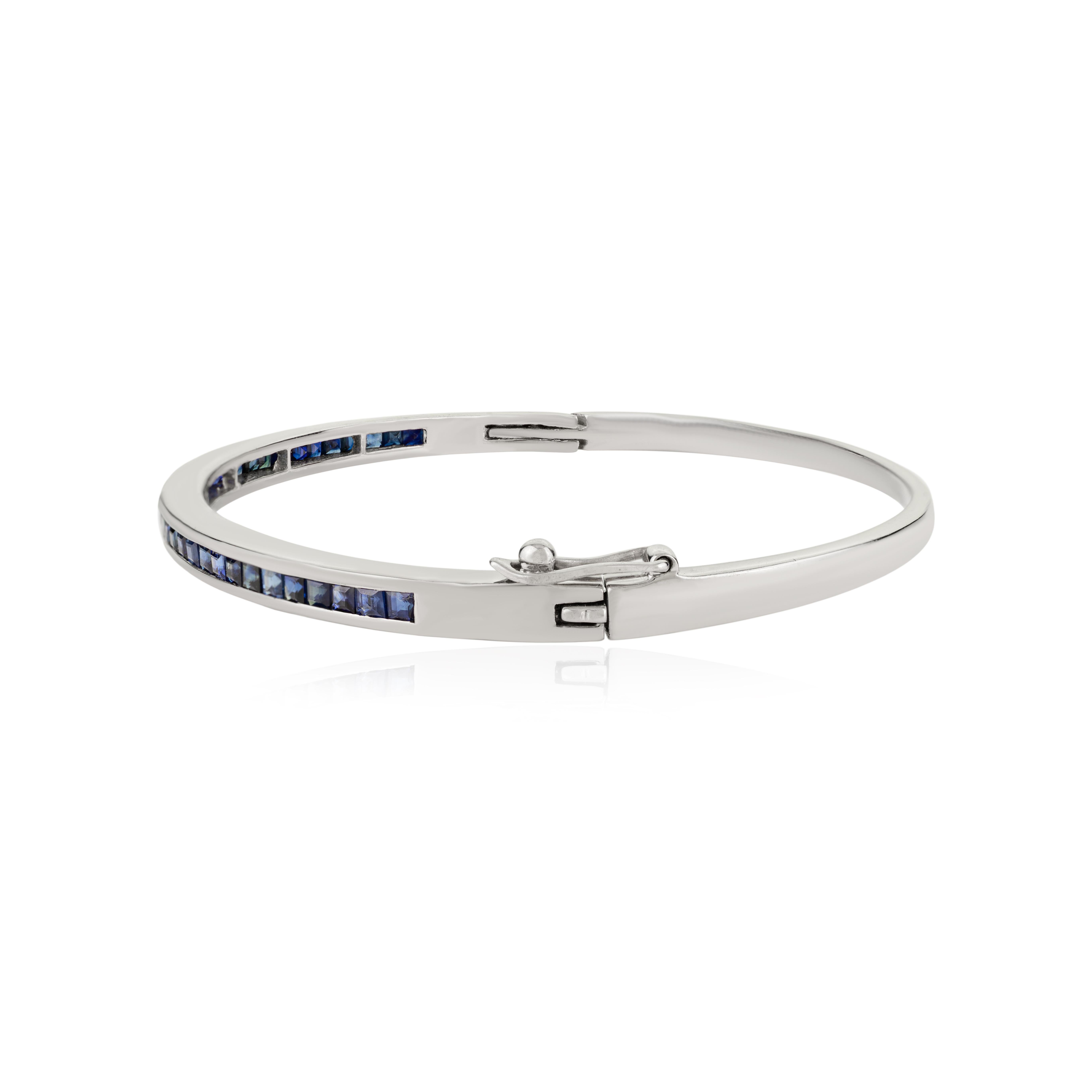 This Channel-Set Blue Sapphire Bangle Bracelet is crafted in 925 sterling silver and adorned with a continuous row of square-cut sapphires, the celebrated birthstone of September. Each deep blue sapphire is precisely channel-set, forming a sleek,