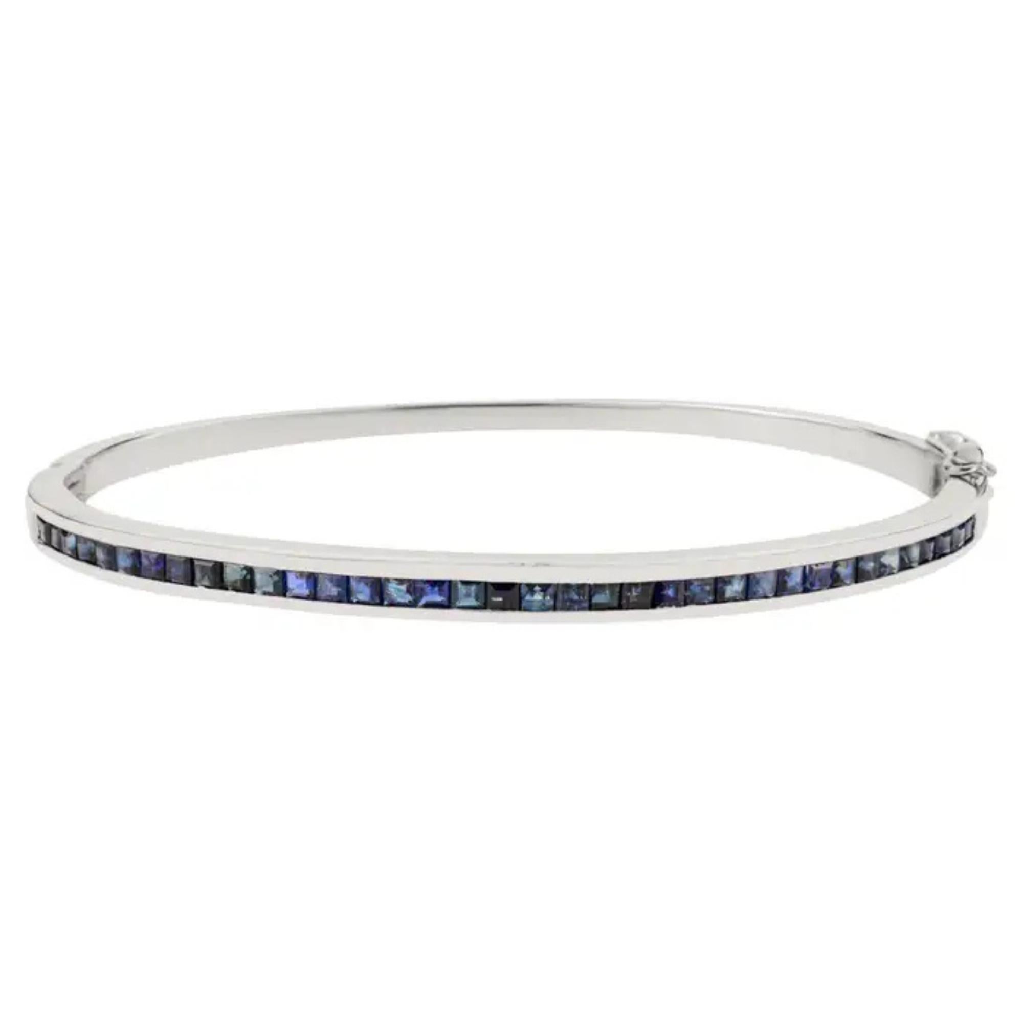 This Channel-Set Blue Sapphire Bangle Bracelet is crafted in 925 sterling silver and adorned with a continuous row of square-cut sapphires, the celebrated birthstone of September. Each deep blue sapphire is precisely channel-set, forming a sleek,