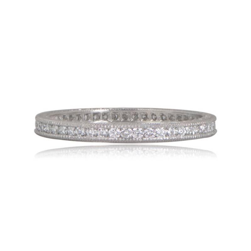 This classic platinum wedding band boasts a captivating antique style with a row of channel-set diamonds. Adorned with beautiful engravings and delicate milgrain details, the top and bottom of the band exhibit timeless elegance. The diamonds,