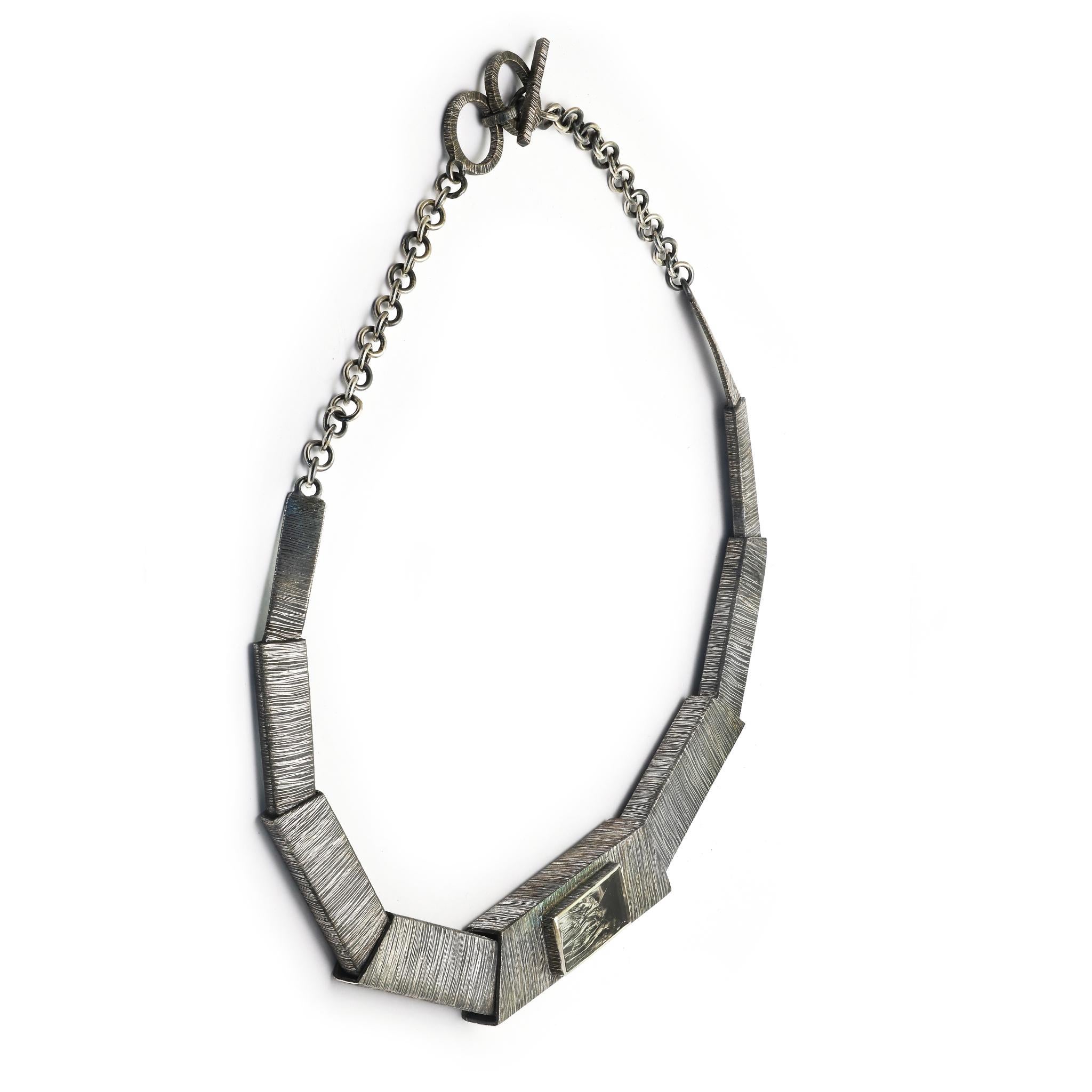 This necklace draws the eye along a channel of variegated rectangles towards the centre piece and the crystal at its heart and the light it reflects through motion.
925 Sterling Silver 
Etched and Oxidized
Free size rectangle shape Rough-Hewn