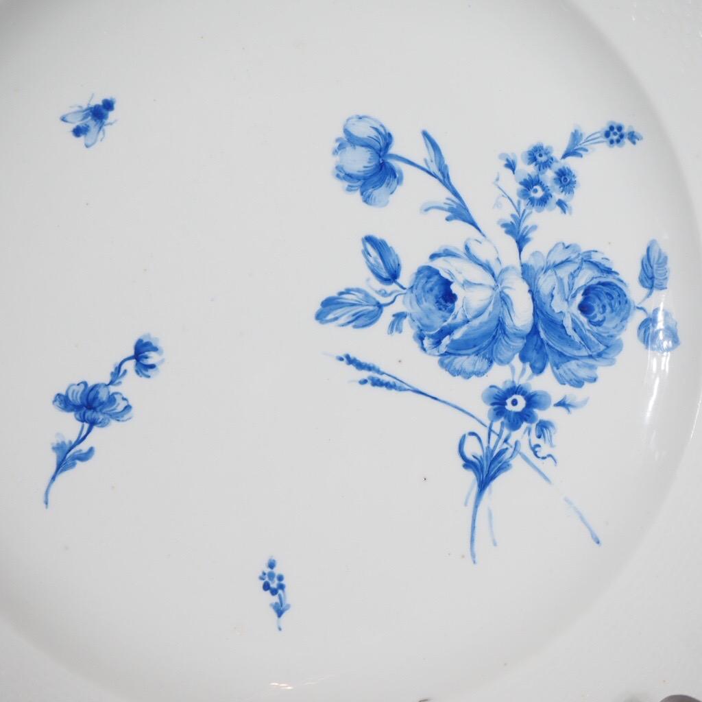 Chantilly plate with lobed basket-weave moulded rim, well painted to the center with a flower group and scattered blooms, a life size fly to one side. 

Blue hunting horn mark and ‘L’, 
also incised hunting horn
Circa 1765.