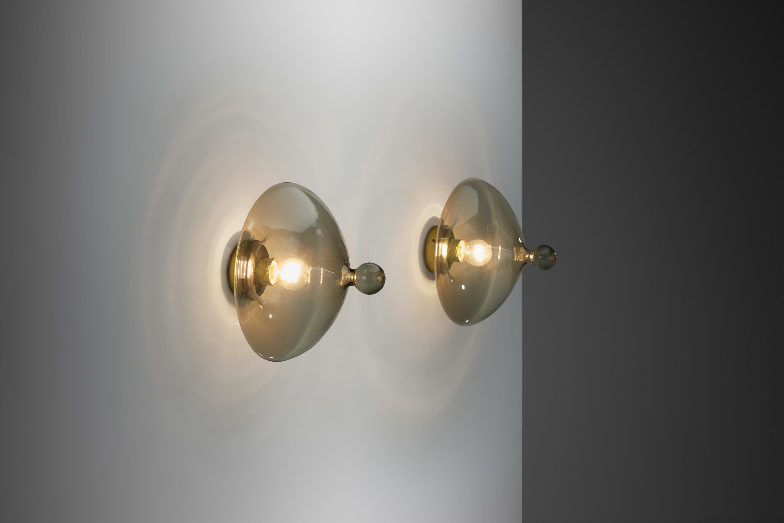 This lovely pair of Dutch ceiling or wall lamps are Raak’s model B-1052, better known as the “Chaparral”. Made of high quality glass with brass details, this model is a unique design that both figuratively and literally stands out wherever it is