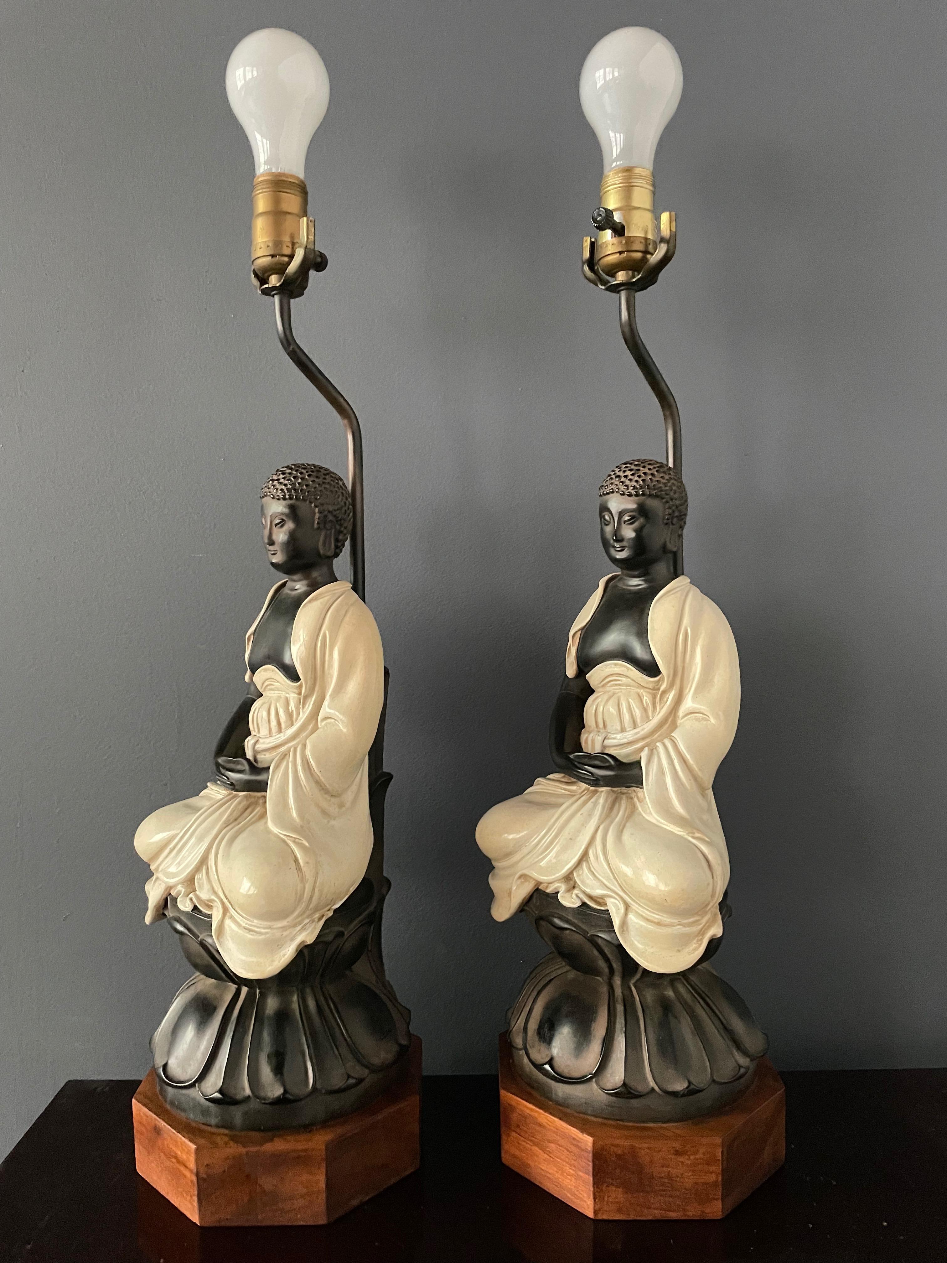 A very interesting pair of ceramic table lamps in the form of a buddha sitting on a rosewood base.