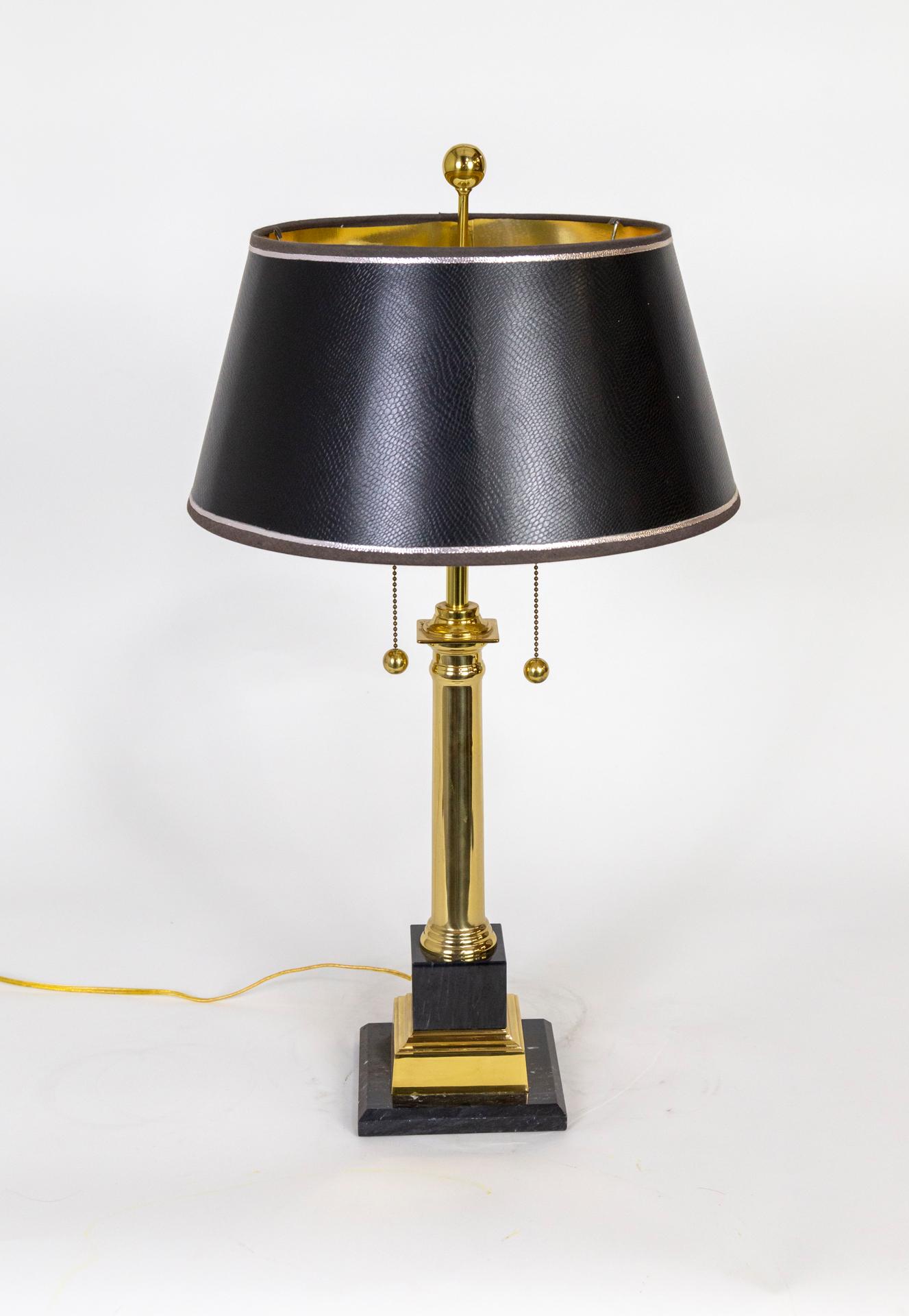A table lamp with a brass column and a stacked black marble and brass base. It is complimented with a slick textured black shade with thin silver trim and a gold interior. It has two pull chains and a double socket.  Circa 1970s. 27.5