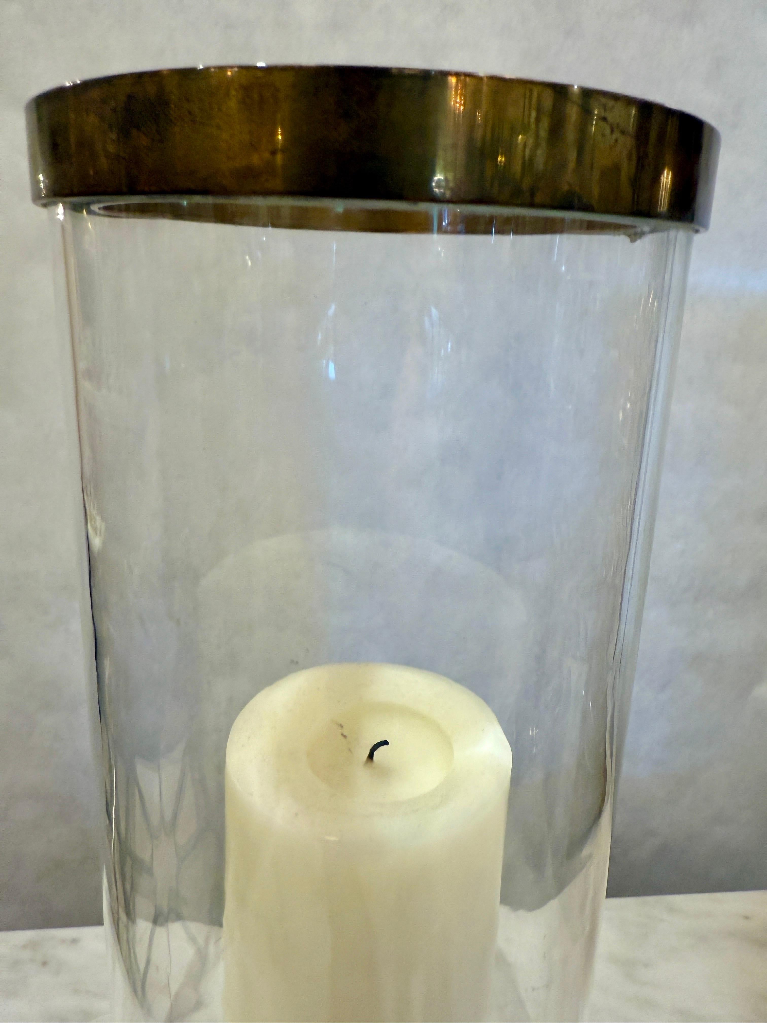 Cette lanterne-tempête élégante et moderne du milieu du siècle est composée d'une base lourde qui accueille une bougie de grande taille, puis d'un cylindre en verre avec un bord en laiton sur le dessus.