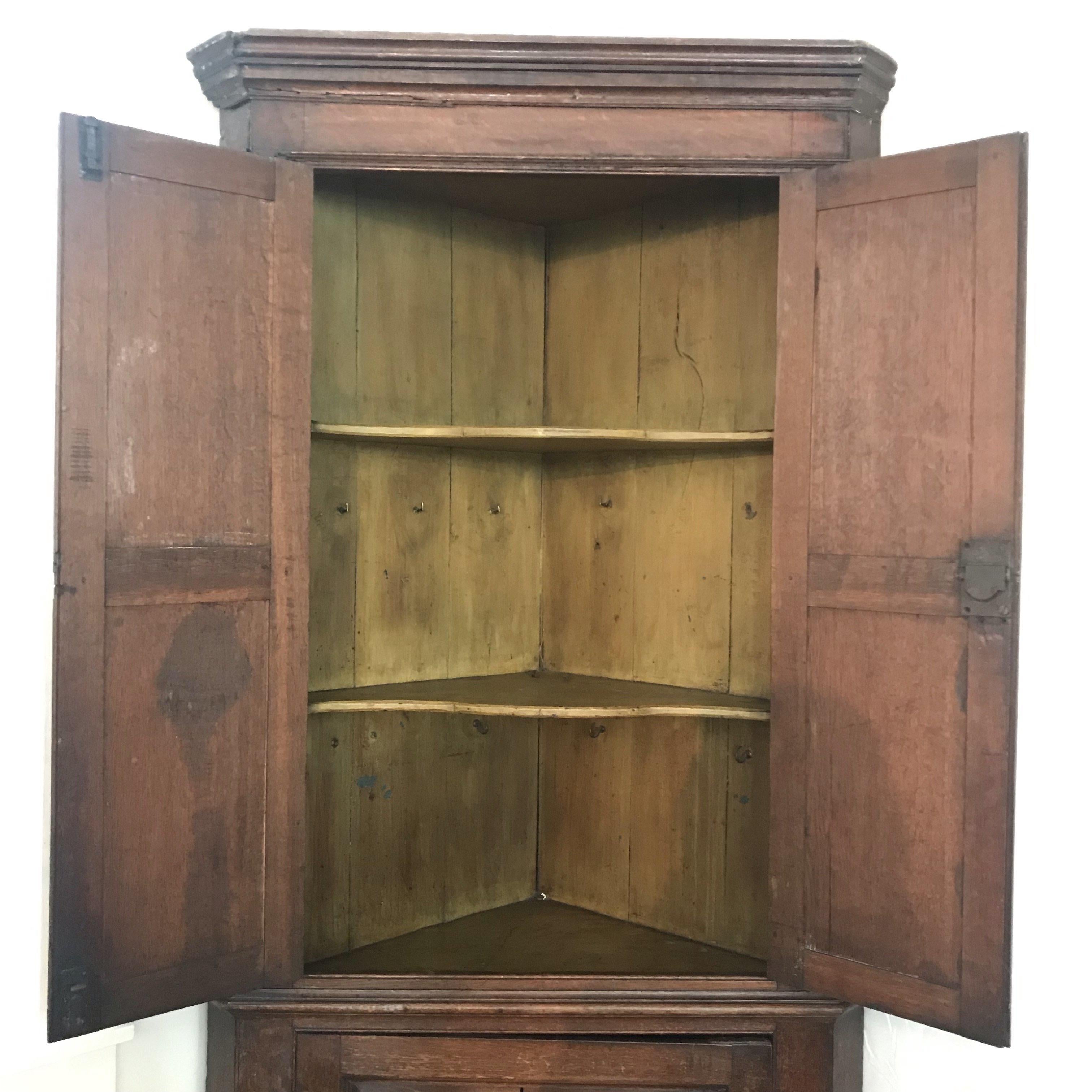 A George III oak double corner cupboard, the top border with classic carved molding, the interior shell shaped with three shelves on the upper section and two on the lower. Bought in the North of England, this super early antique Georgian British