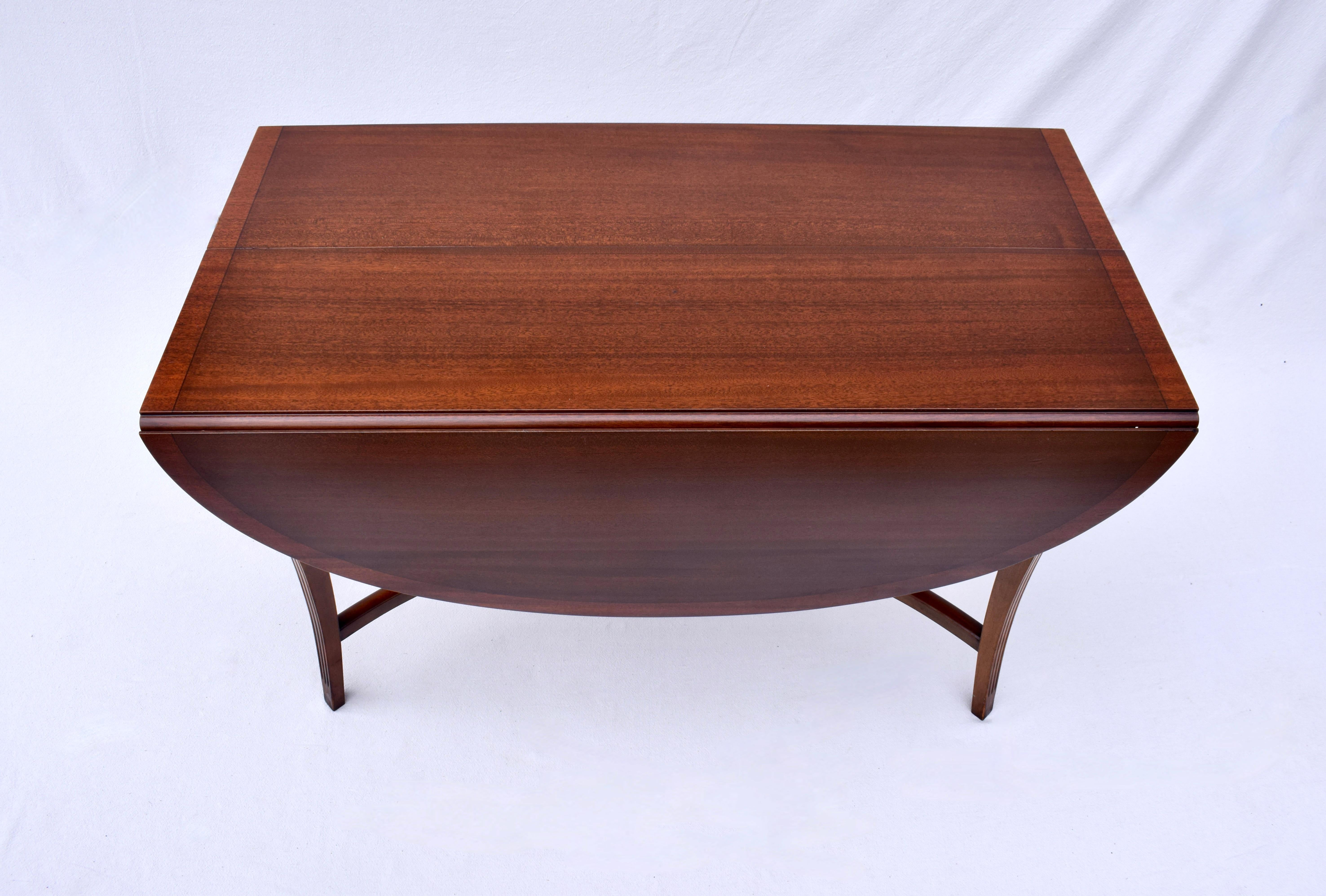 Elegant Charak Danbury drop leaf table featuring banded mahogany border with vibrant mahogany grains, Incised detail to the canted saber legs and exquisite X stretcher that mirrors the curves of the drop sides. Leaves extended, the top pivots 180