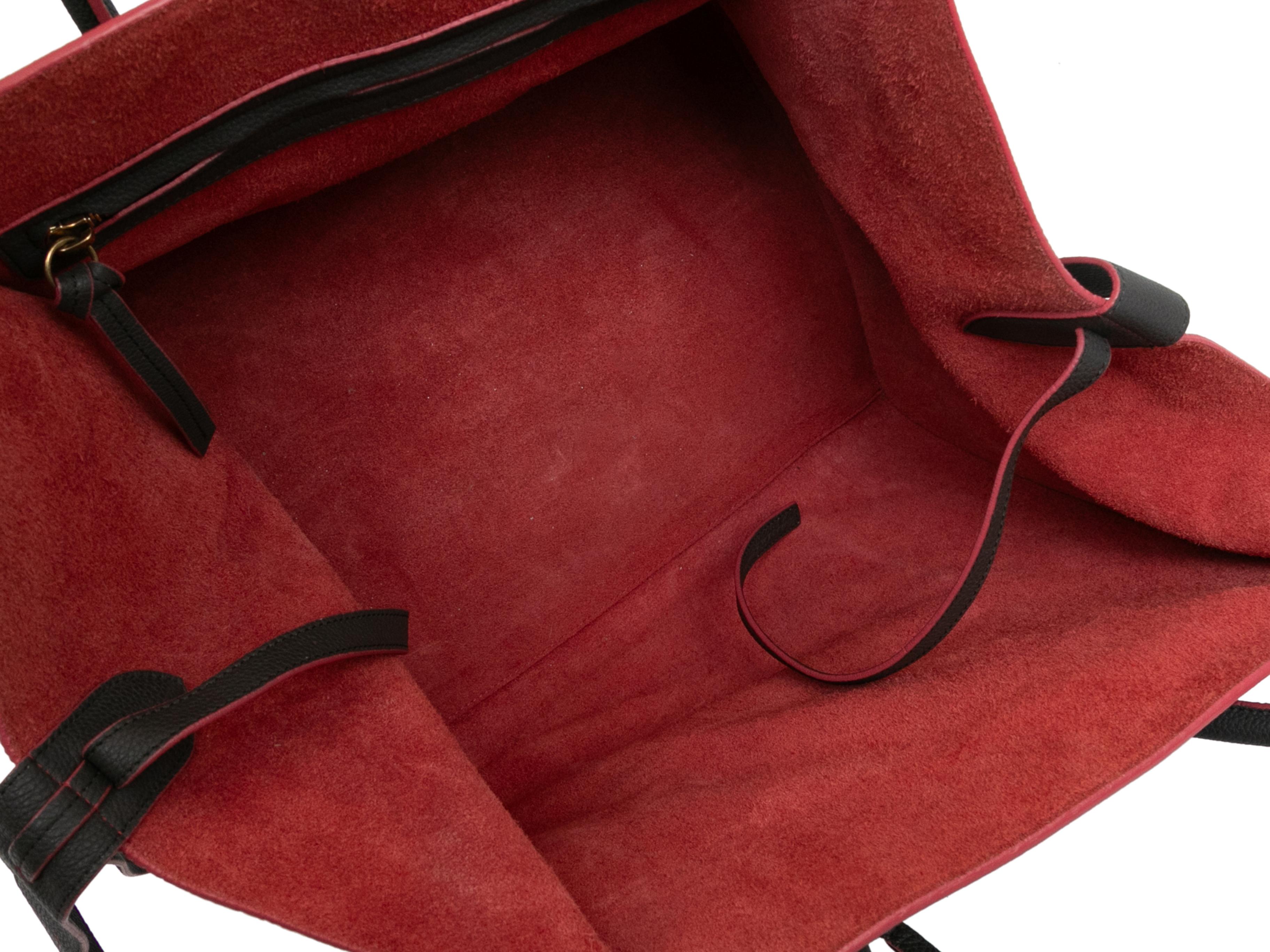 Kleine Phantom-Gepäcktasche in Holzkohle und Rot. Die kleine Phantom-Gepäcktasche hat einen Korpus aus Leder, eine Innenausstattung aus Wildleder, goldfarbene Beschläge, eine Reißverschlusstasche auf der Vorderseite und zwei gerollte Griffe oben.