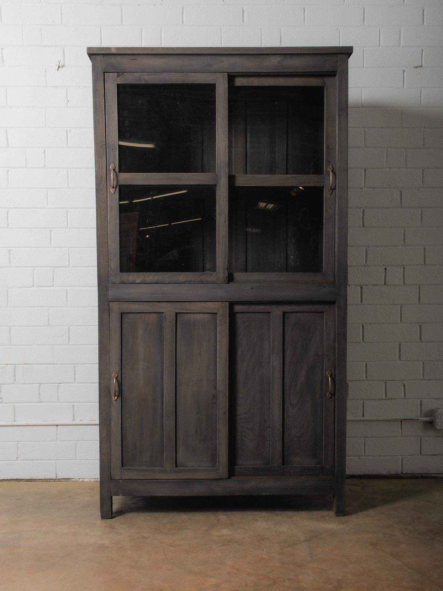 A grounded, architectural form rendered in a deep charcoal wash, this cabinet balances transparency and solidity through its dual composition of glass-front doors above and paneled doors below. The silhouette is calm and assured—rectilinear,